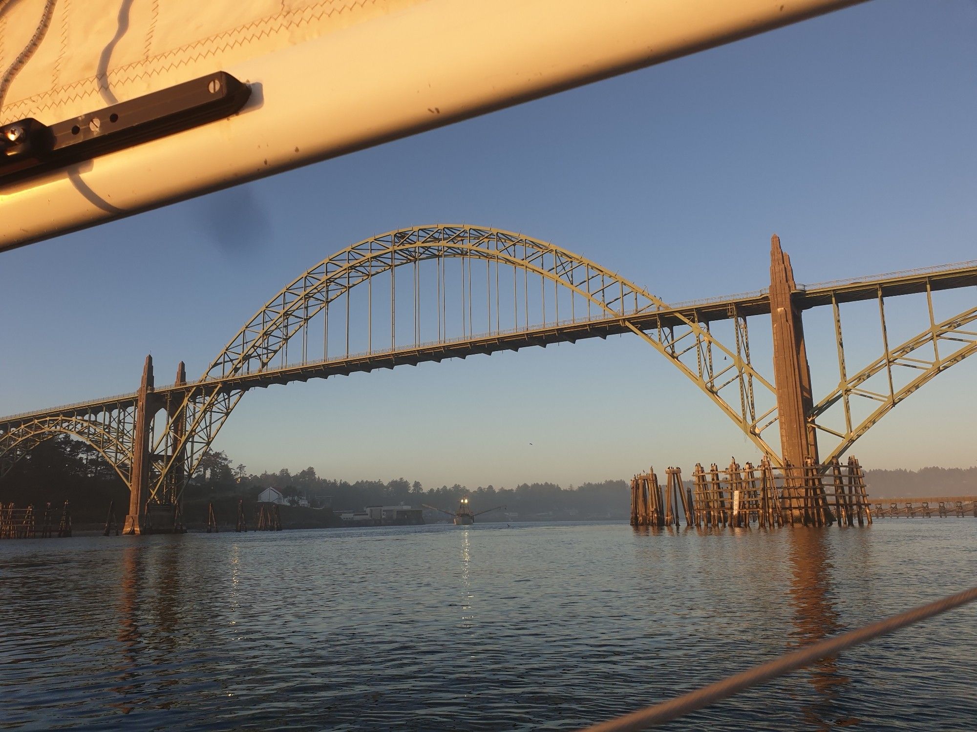 Yaquina Bay Bridge, with a fishing boat heading out under, lit by low sun