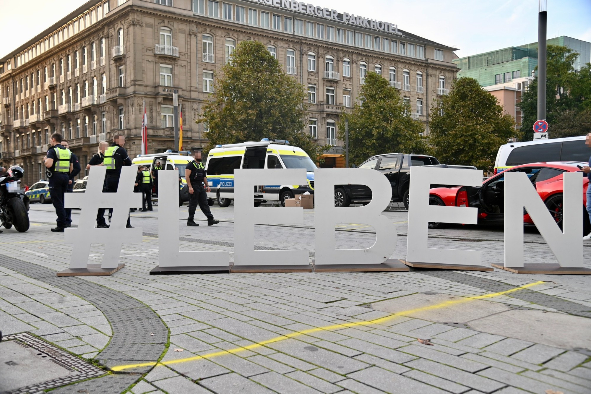 Pappaufsteller #LEBEN quer auf einem Radweg, dahinter ist das Piktogramm zu erkennen, im Hintergrund Polizei