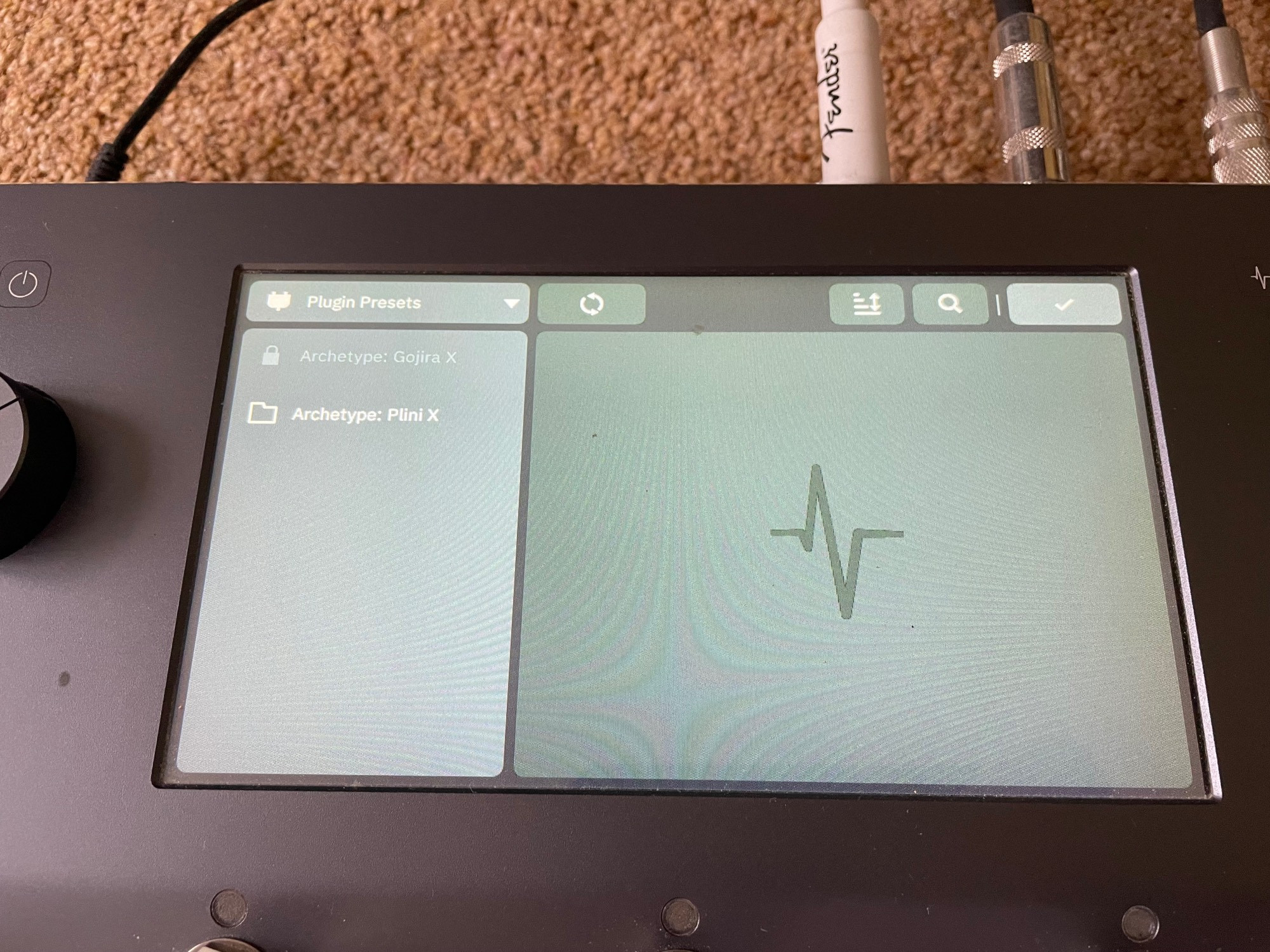 A NeuralDSP Quad Cortex sat on the floor, and a closeup of the touchscreen display which is showing the available Plugins, with the “Archetype: Plini X” plugin appearing as unlocked.