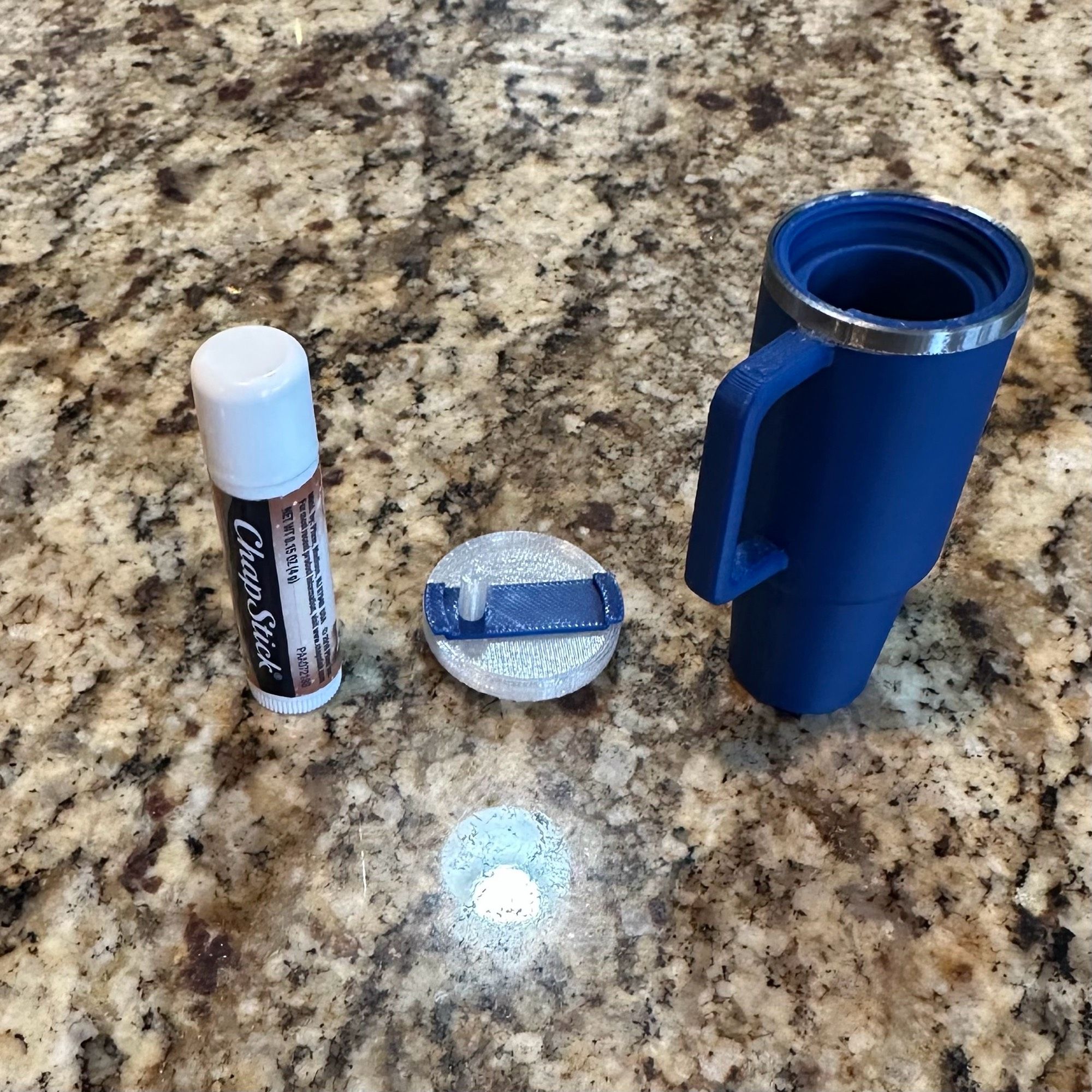 A chapstick, a translucent 3D printed Stanley cup lid with a blue accent, and a blue 3D printed Stanley mug with silver rim, about 2 inches high