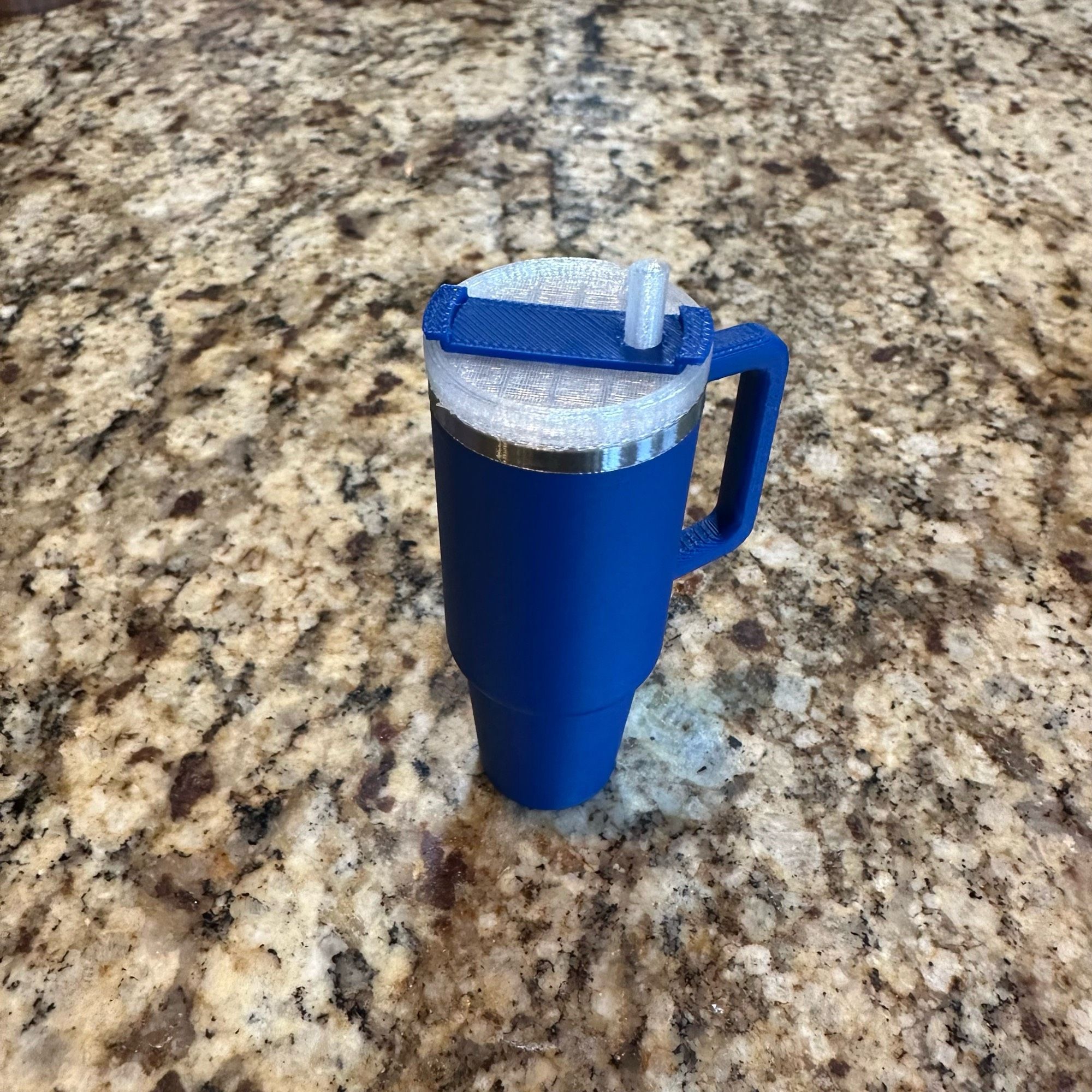 A blue 3D printed Stanley mug with silver rim with translucent lid screwed on containing a chapstick