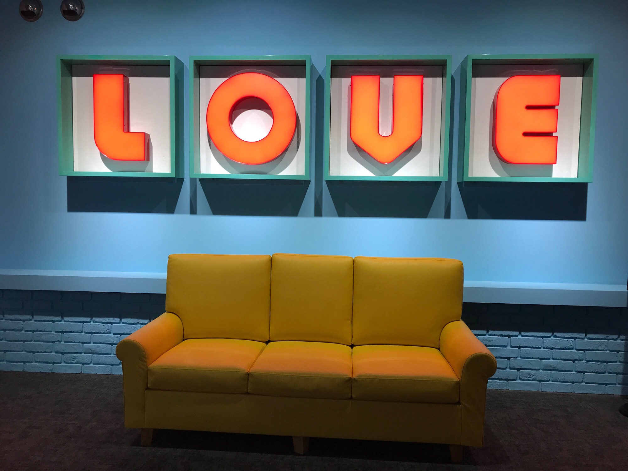 The Boy With Love couch set with the neon sign LOVE in the back