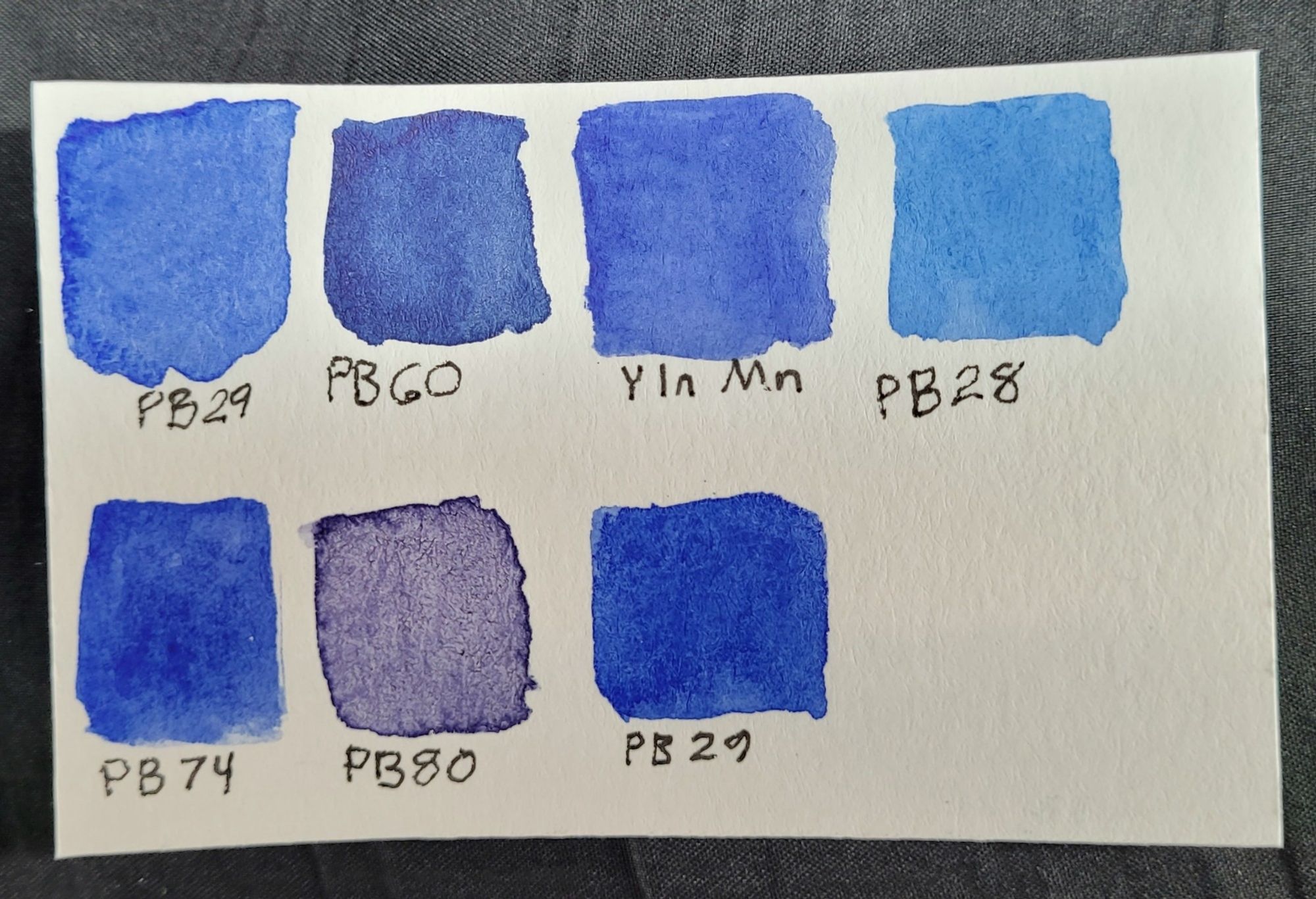 Small piece of watercolor paper with blue paint swatches for: PB29 (ultramarine), PB60 (Indanthrone blue), Y In Mn blue, PB 28 (cobalt), 
PB 74 (cobalt blue dark), PB 80 (Benzimidazo blue R5R), and another PB 29. 