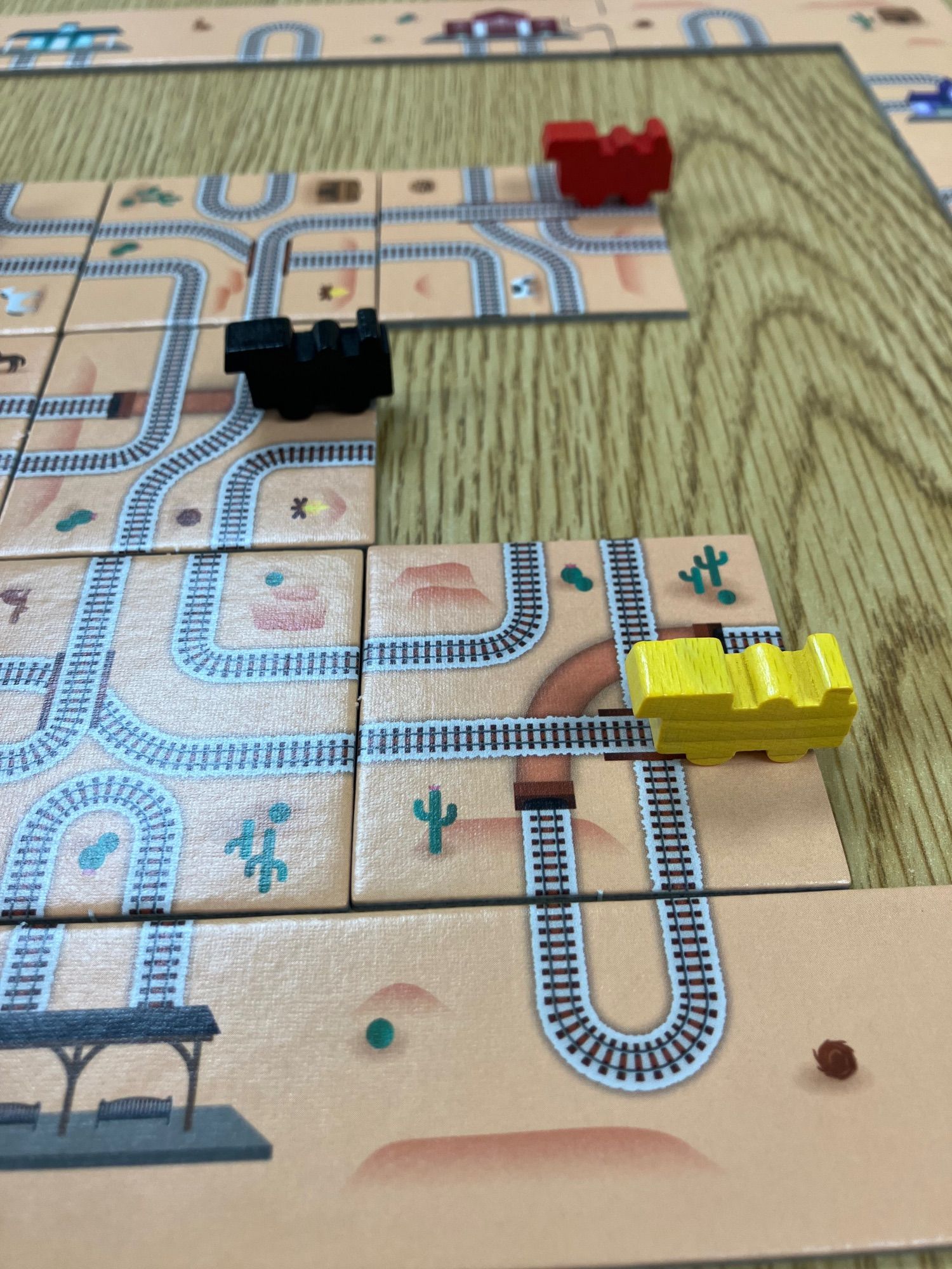 A closeup of the board game “Twisty Tracks” featuring orange tiles with train tracks on them and wooden train pieces on them