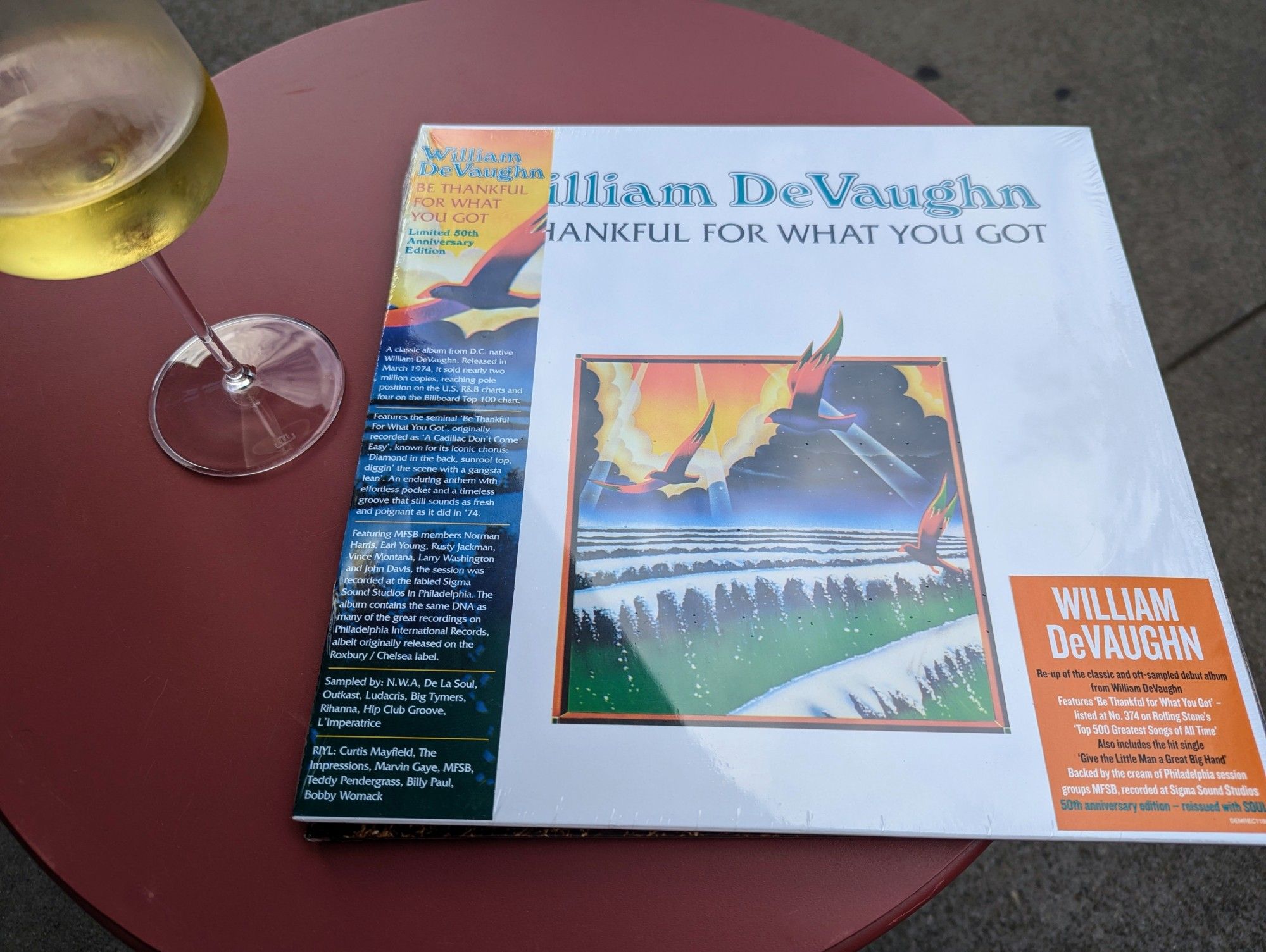 A freshly reissued copy of William DeVaughan's "Be Thankful For What You Got" next to a glass of white wine. 