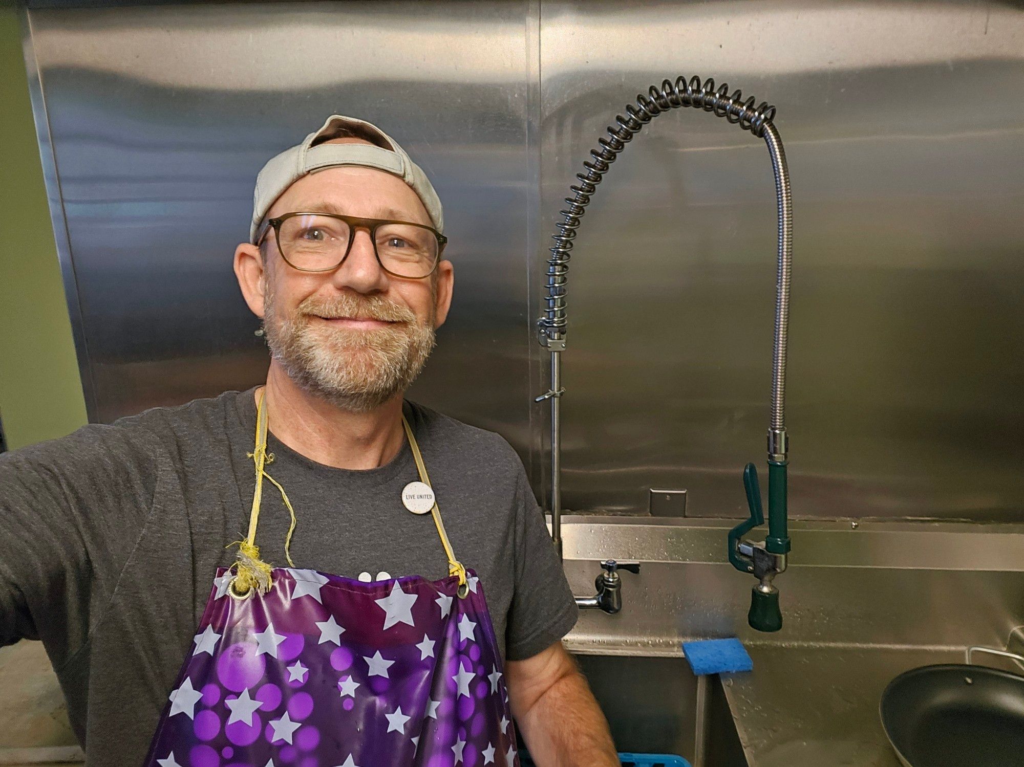 Me, wearing a purple apron with white stars, taking a selfie in the dish cleaning area.