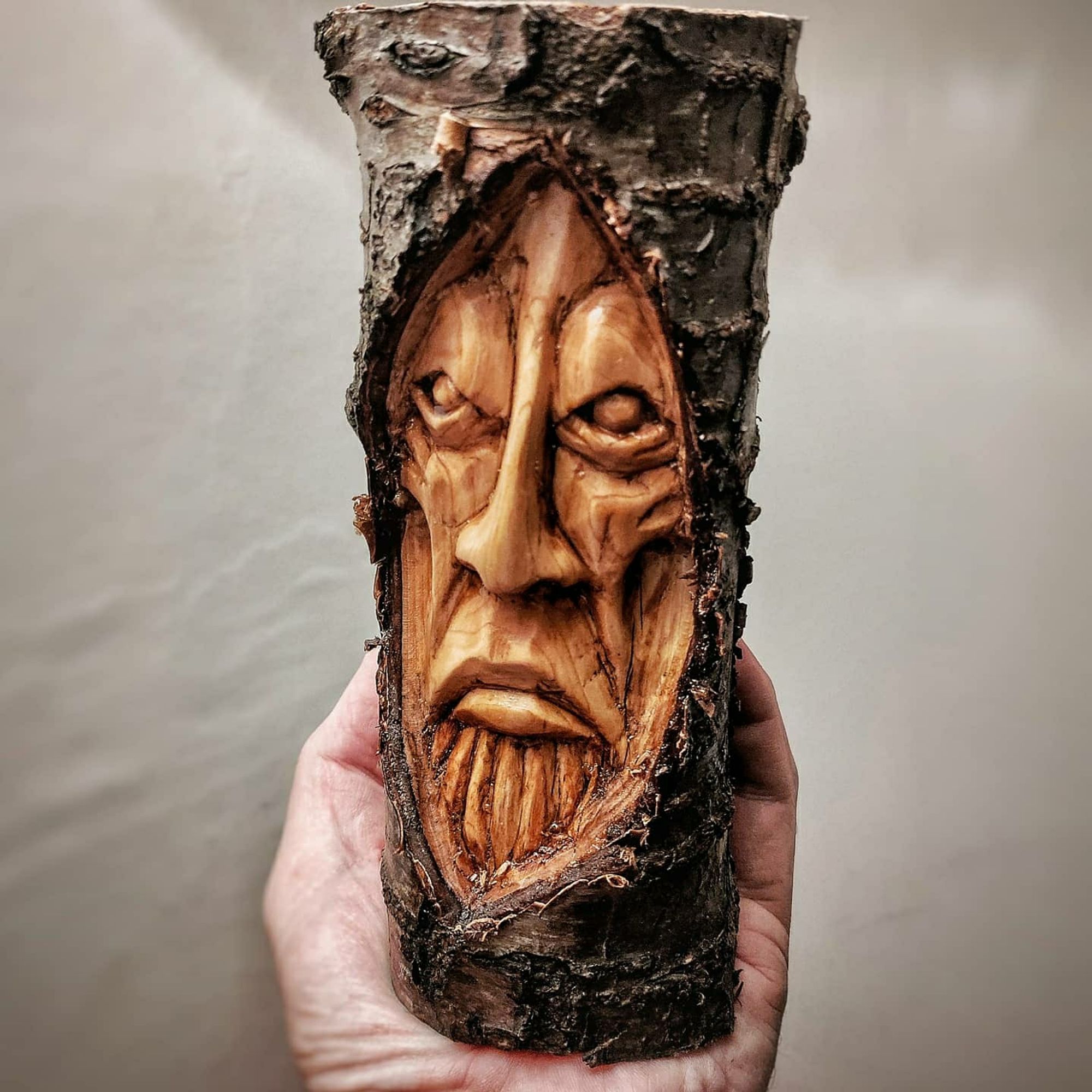 Section of a cherry tree branch with a grumpy face carved into one side 