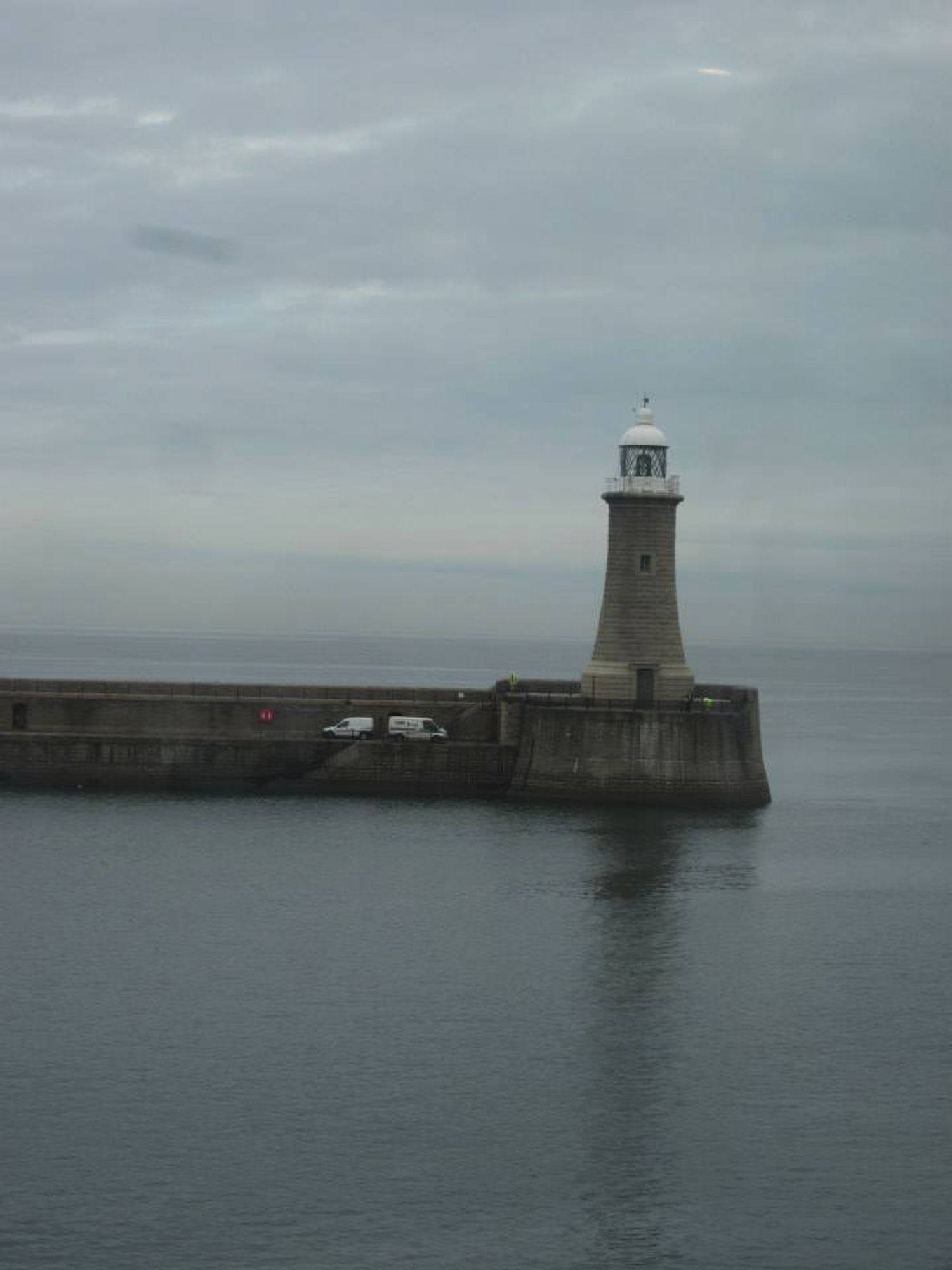 Grey skies and grey water, and a small lighthouse with a white top.