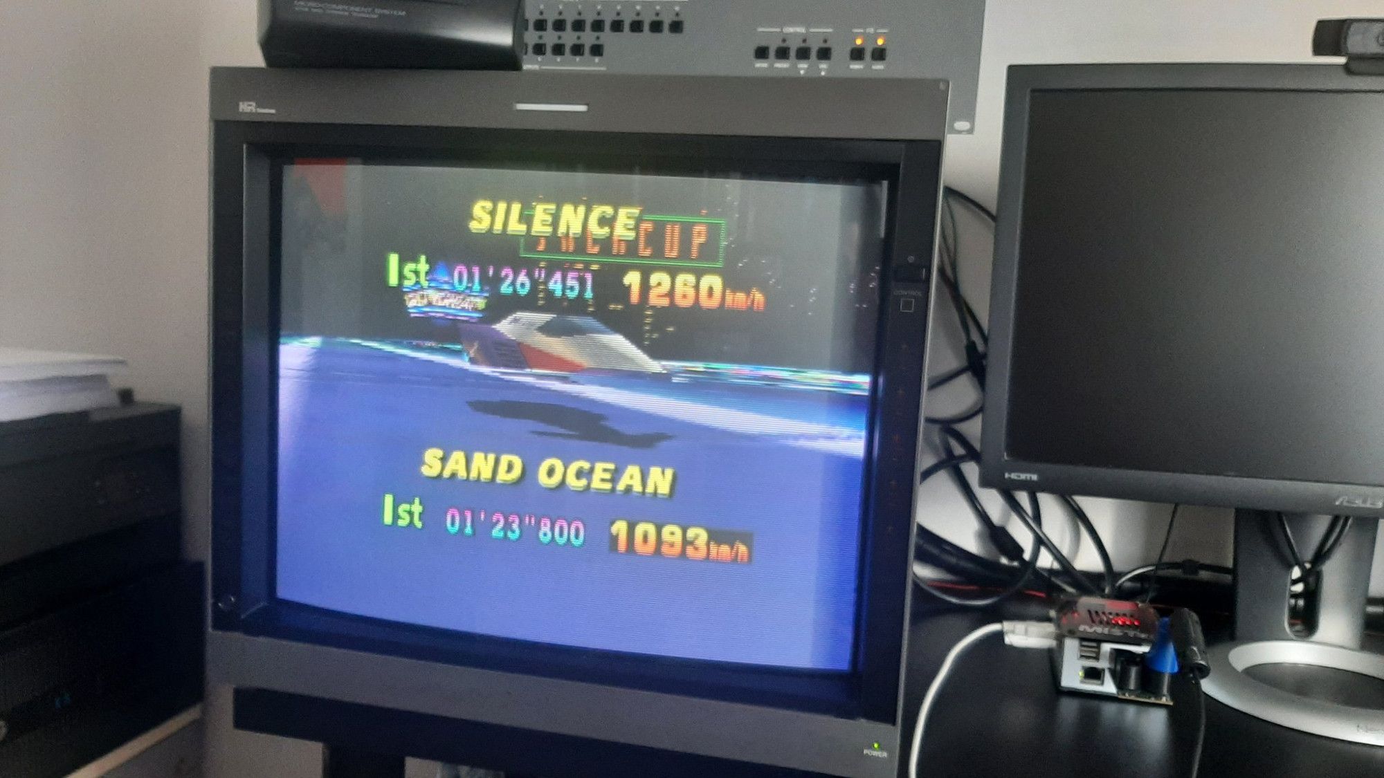 F-Zero X, an sci-fi racing game, is displayed on a CRT monitor. Cables can be seen in the background.