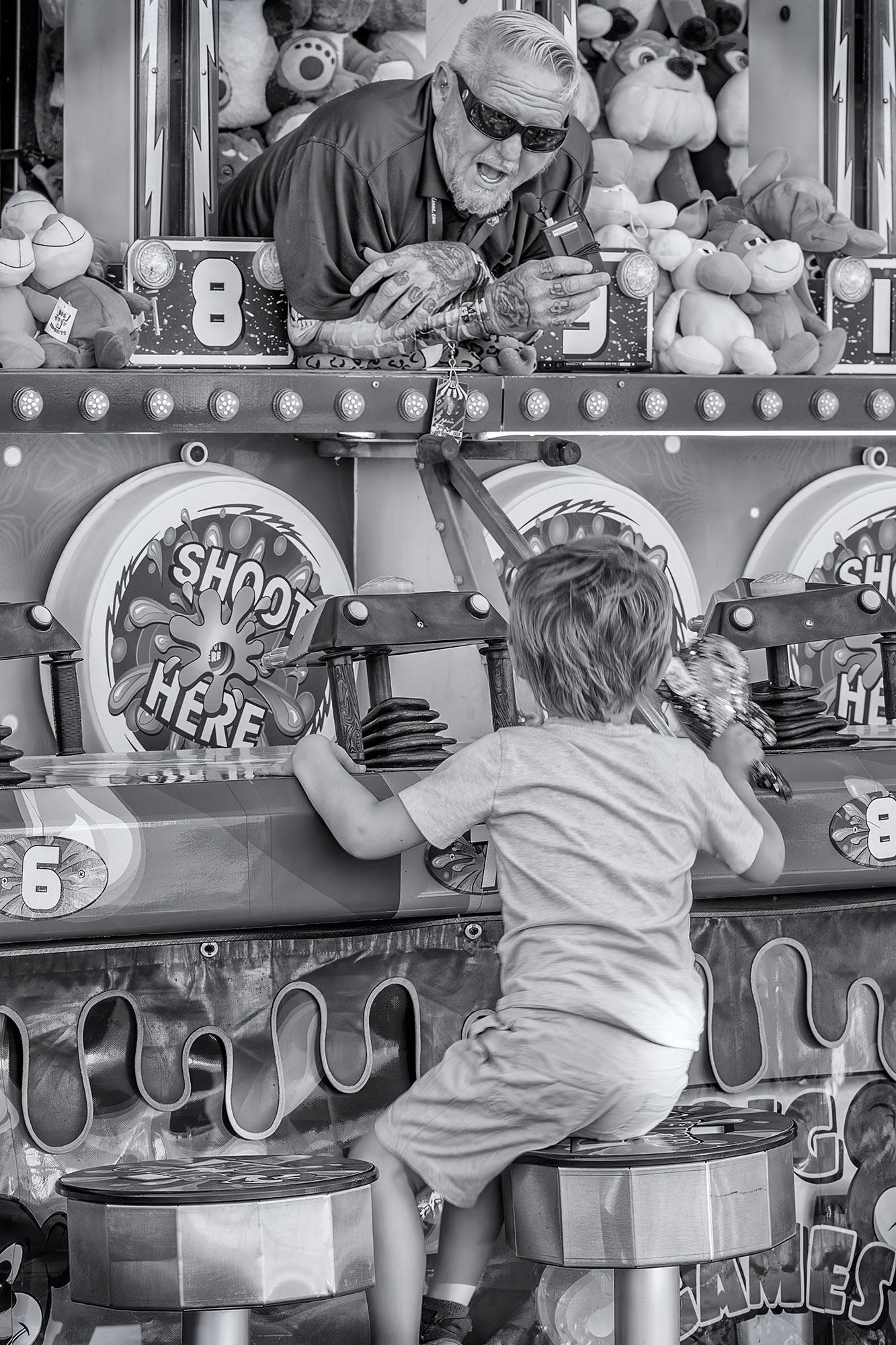 Carnival game operator bends down over counter to talk to boy who has come to play shooting gallery type game at the Napa County Fair.