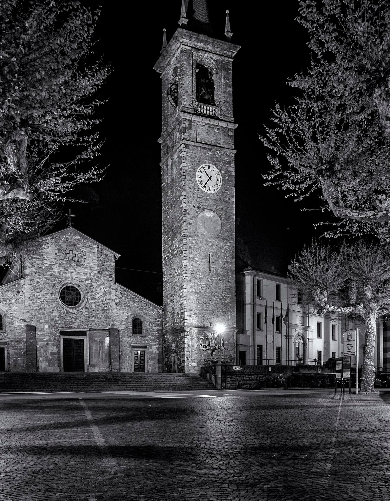 Cobblestone courtyard in front of church with bell tower in a small town bordering Lake Como in Italy.