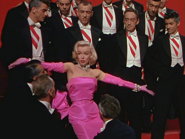 Marilyn Monroe as Lorelei Lee performs "Diamonds Are a Girl's Best Friend" in Gentlemen Prefer Blondes. She wears a hot pink satin gown and is surrounded by handsome men in black and white suits with red and white striped ties (exactly like the Kens in the previous photo).