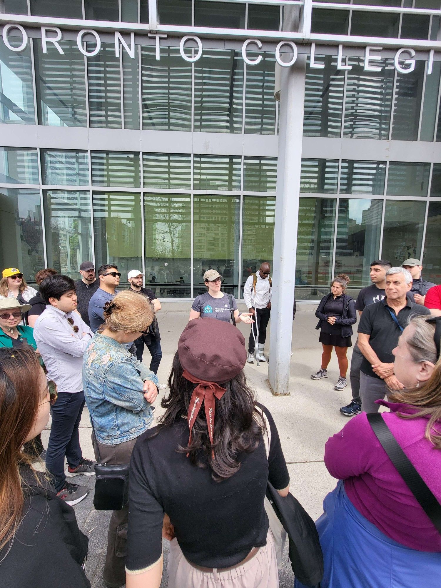 A group of people on a pedestrian path. A large glass wall is behind them, reflecting some tall buildings. Part of the "North Toronto Collegiate Institute" sign can be seen above them.