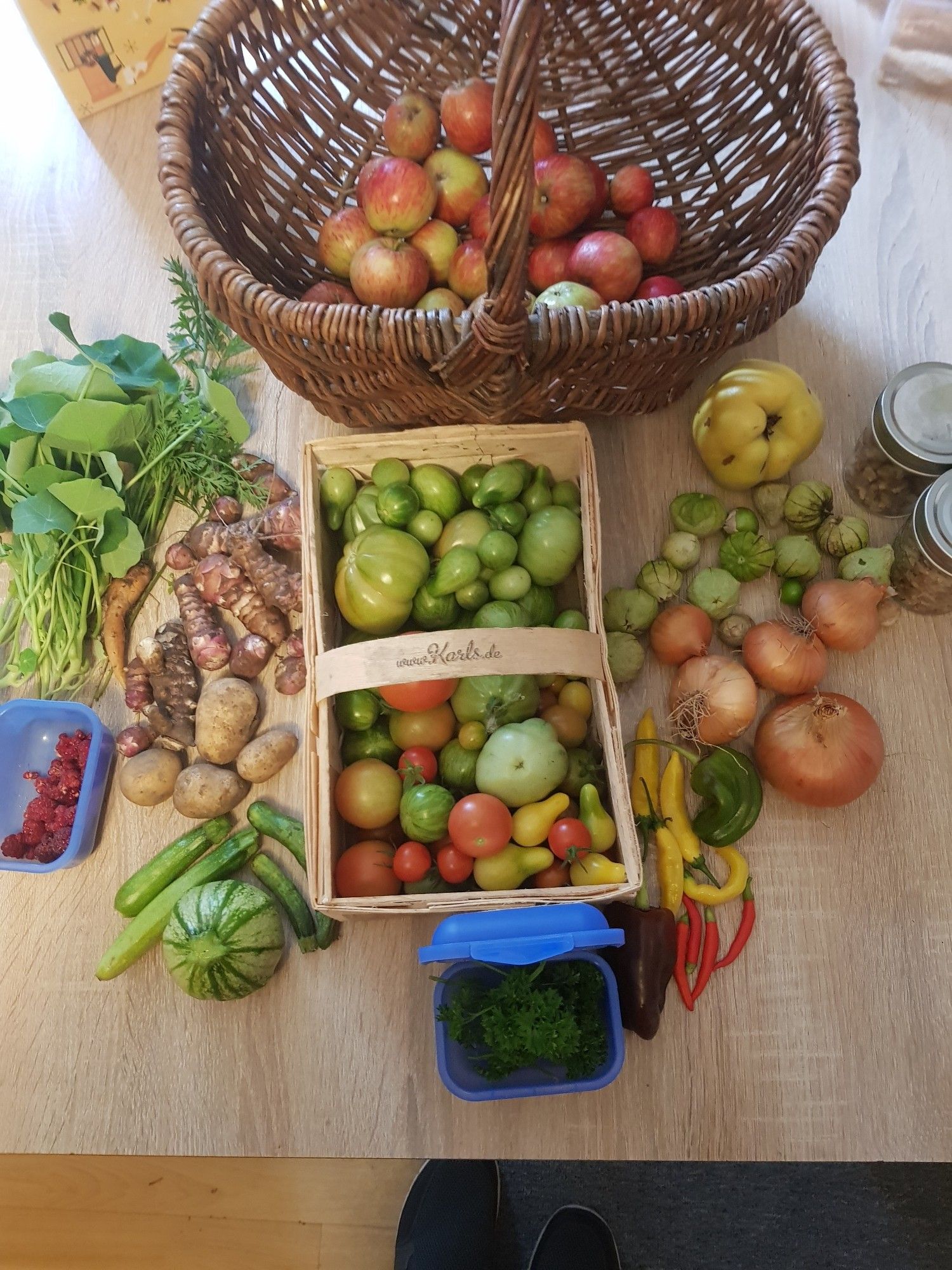 Auf dem Tisch stehen Äpfel, Tomaten welche meist nachreifen müssen, Topinambur, Kartoffeln, Chili und Paprika, kleine Zucchini, paar Himbeeren verschiedene Kräuter, fünf Zwiebeln und zwei Gläser mit Wallnusskernen.