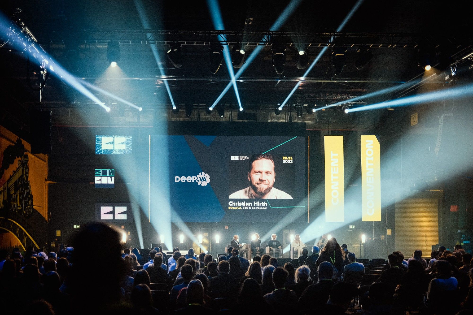 Image of a big crowd in front of a stage with a picture of CEO Christian Hirth from DeepVA on screen.