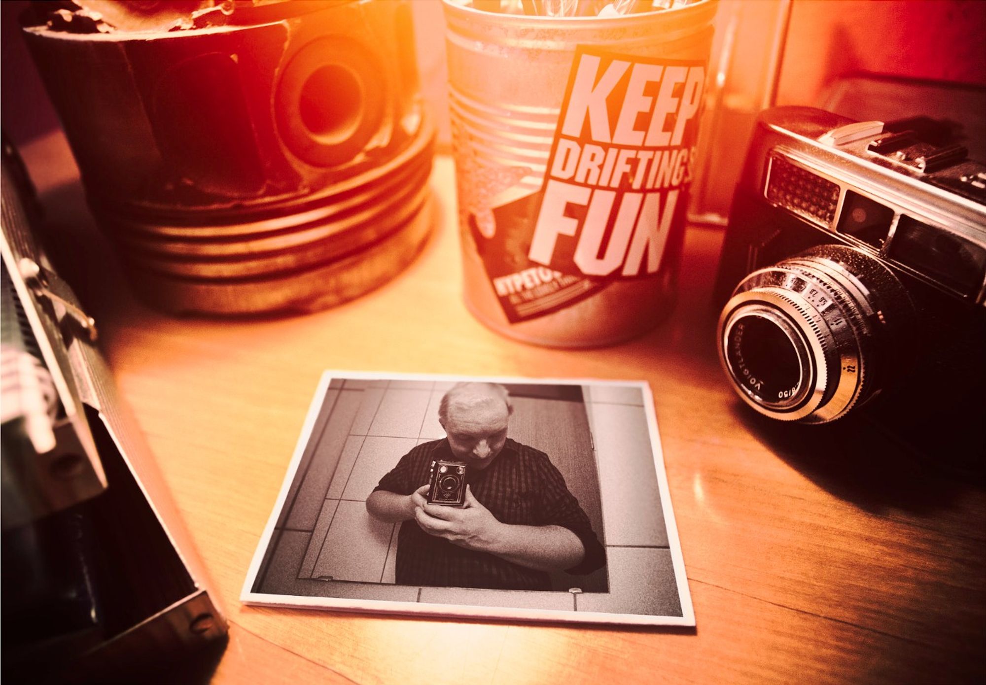 Close-up of a desk with an old camera, some car related parts and a selfie portrait of Fabian Linder made with a 4x5 midformat camera