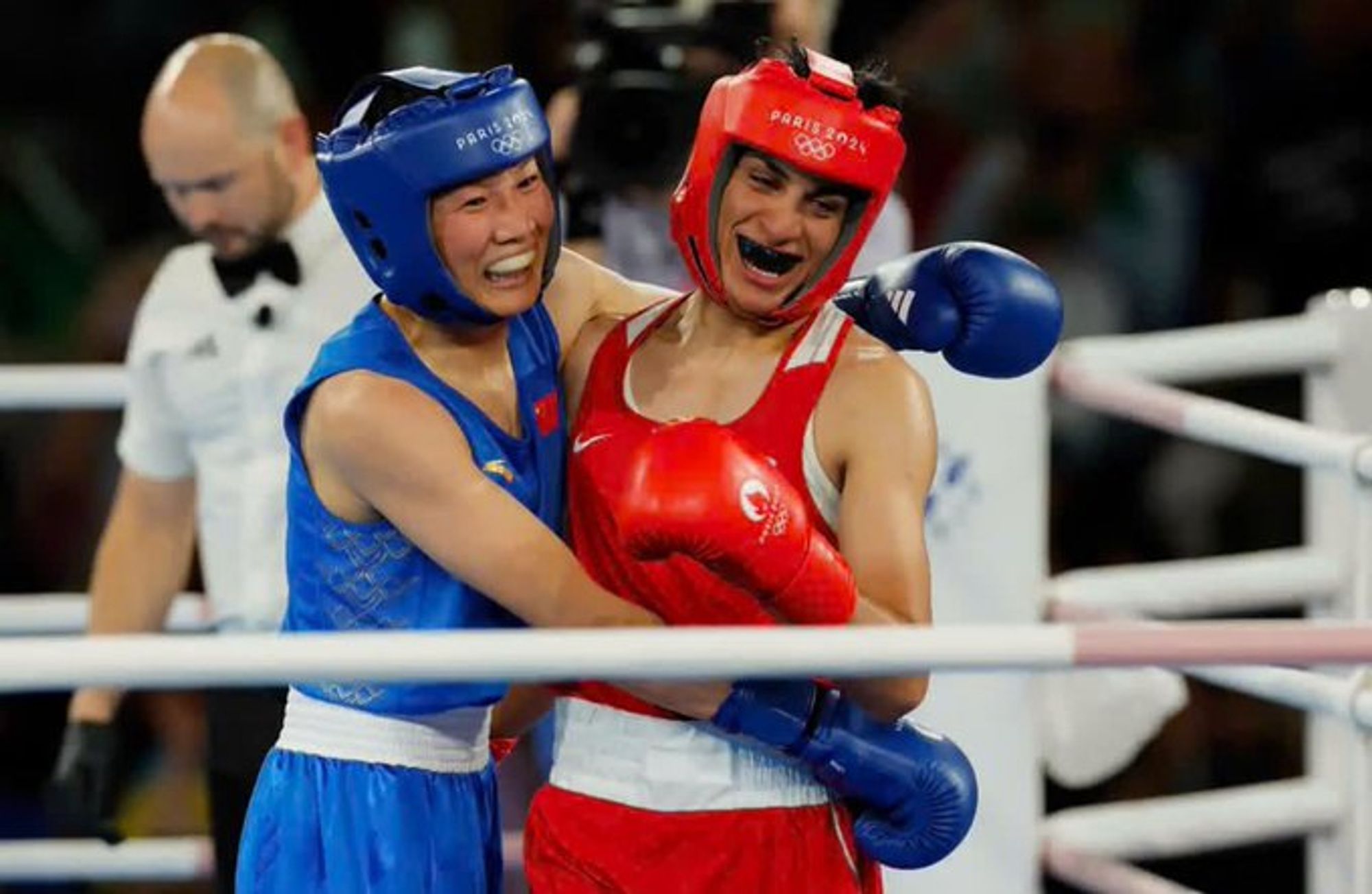 Deux boxeuses, Imane Khelif en rouge, avec son protège dents noir, et Yang Liu en bleu, s'étreignent après le match, visiblement fatiguées mais euphoriques.