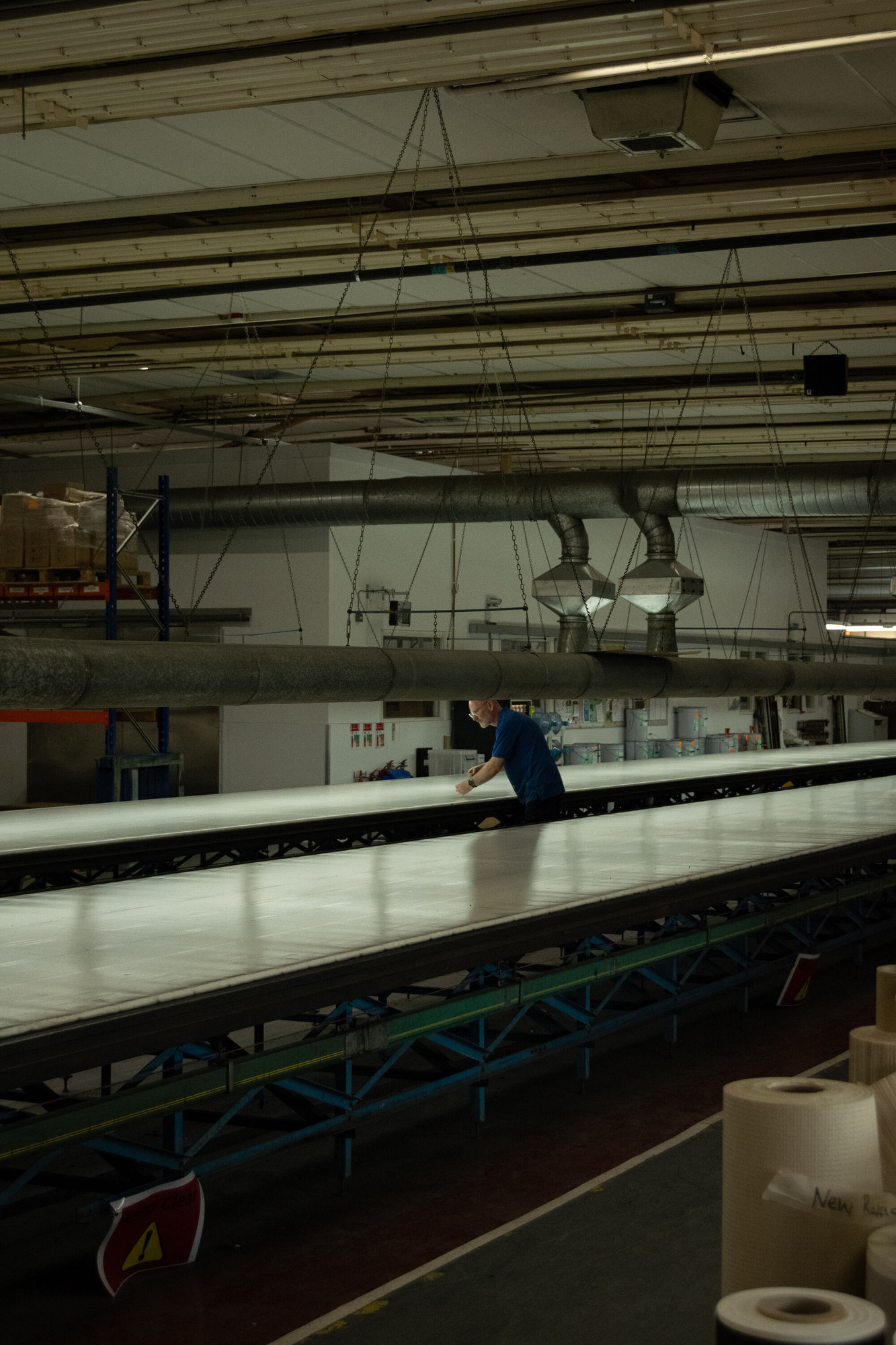 View of wallpaper-making machinery with a worked in the middle, his back turned to the viewer.