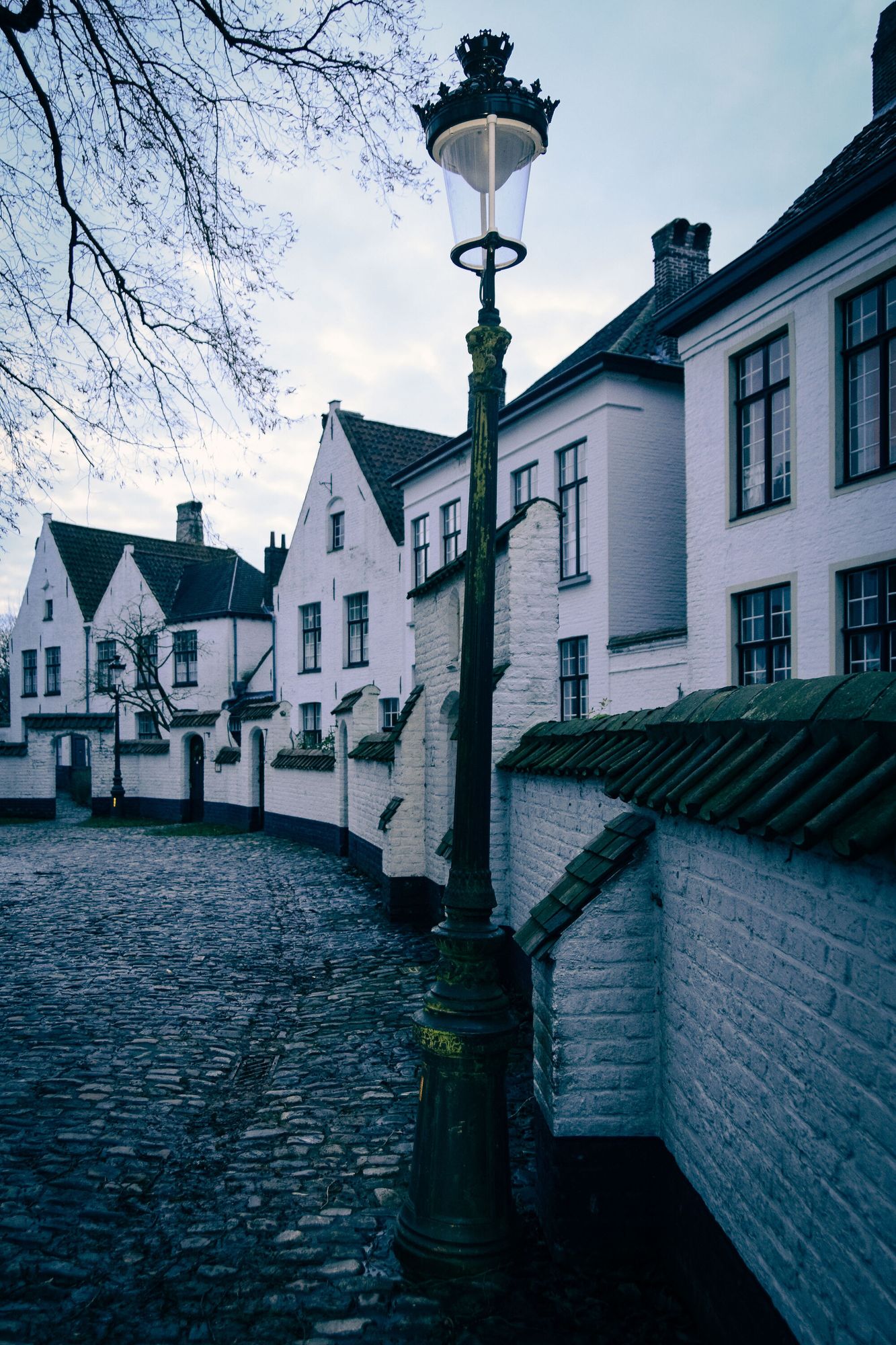 A lamppost on a cobbled street; old white brick houses at dusk.