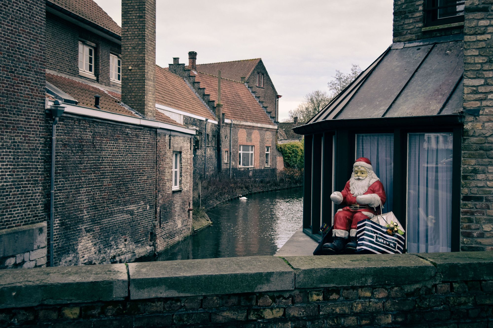 Houses alongside a canal; a Santa Claus is sitting on the window ledge near the bridge.