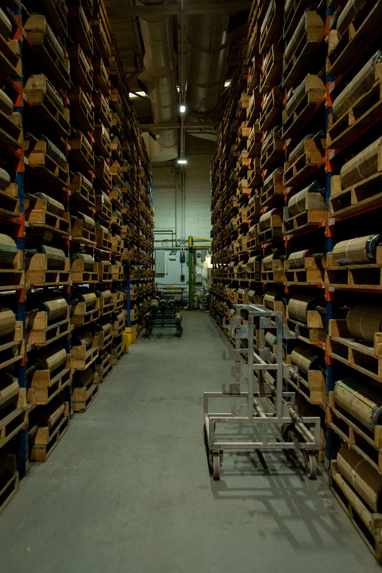 View down a warehouse isle with printing rolls stored on pallets on either side.