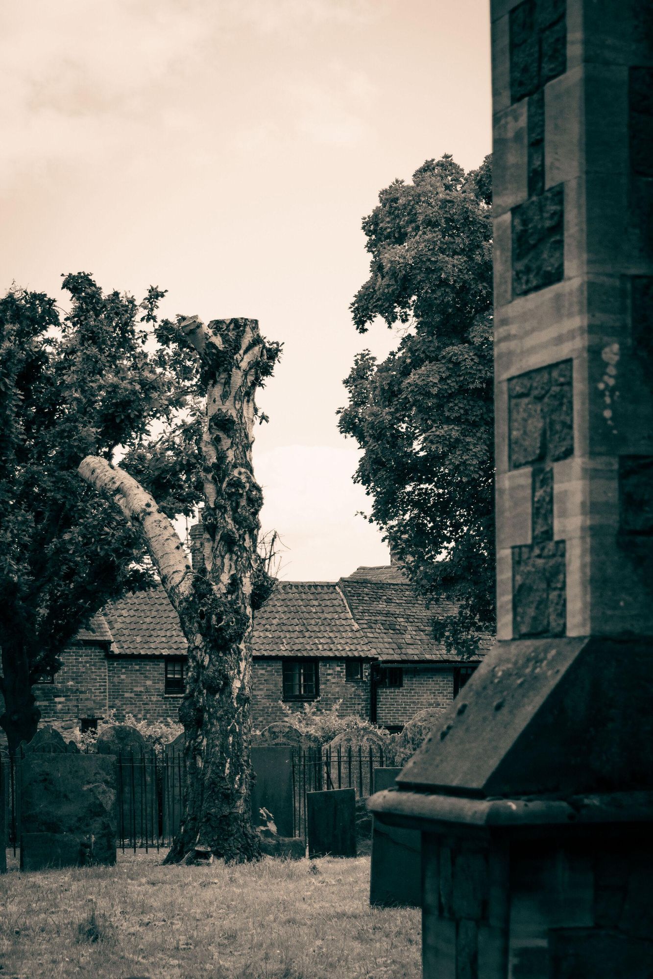 In the foreground is the side of the church; further in the back are a tree and some old houses.