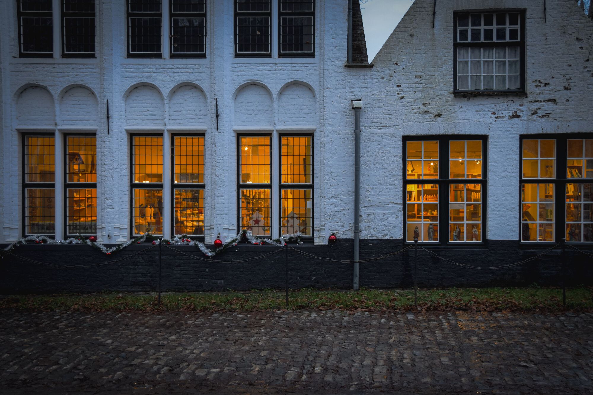 White houses on a cobbled street with lights by the windows at dusk