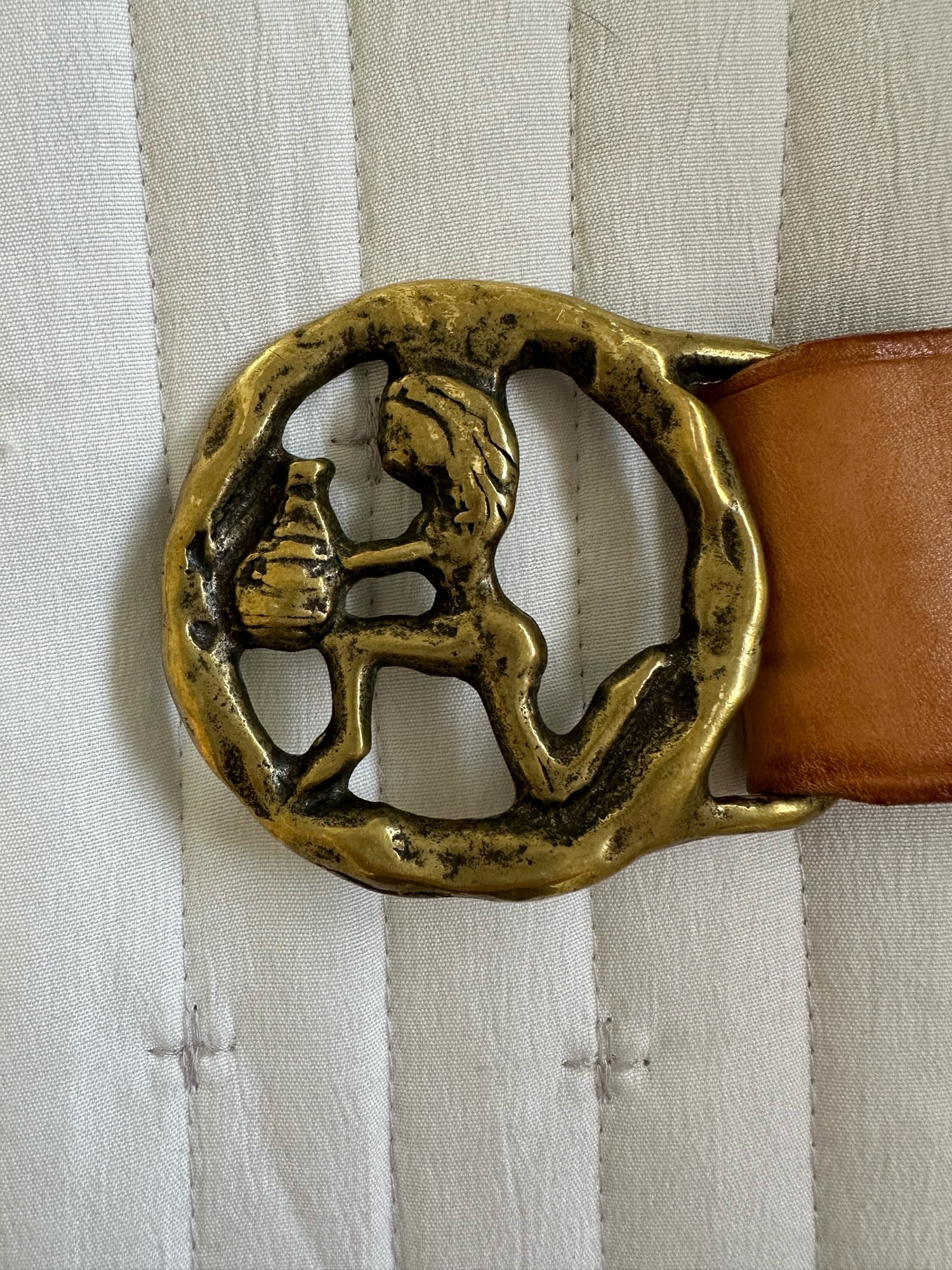 A brass belt buckle. It’s a circle with a person on one knee holding a basket or something?