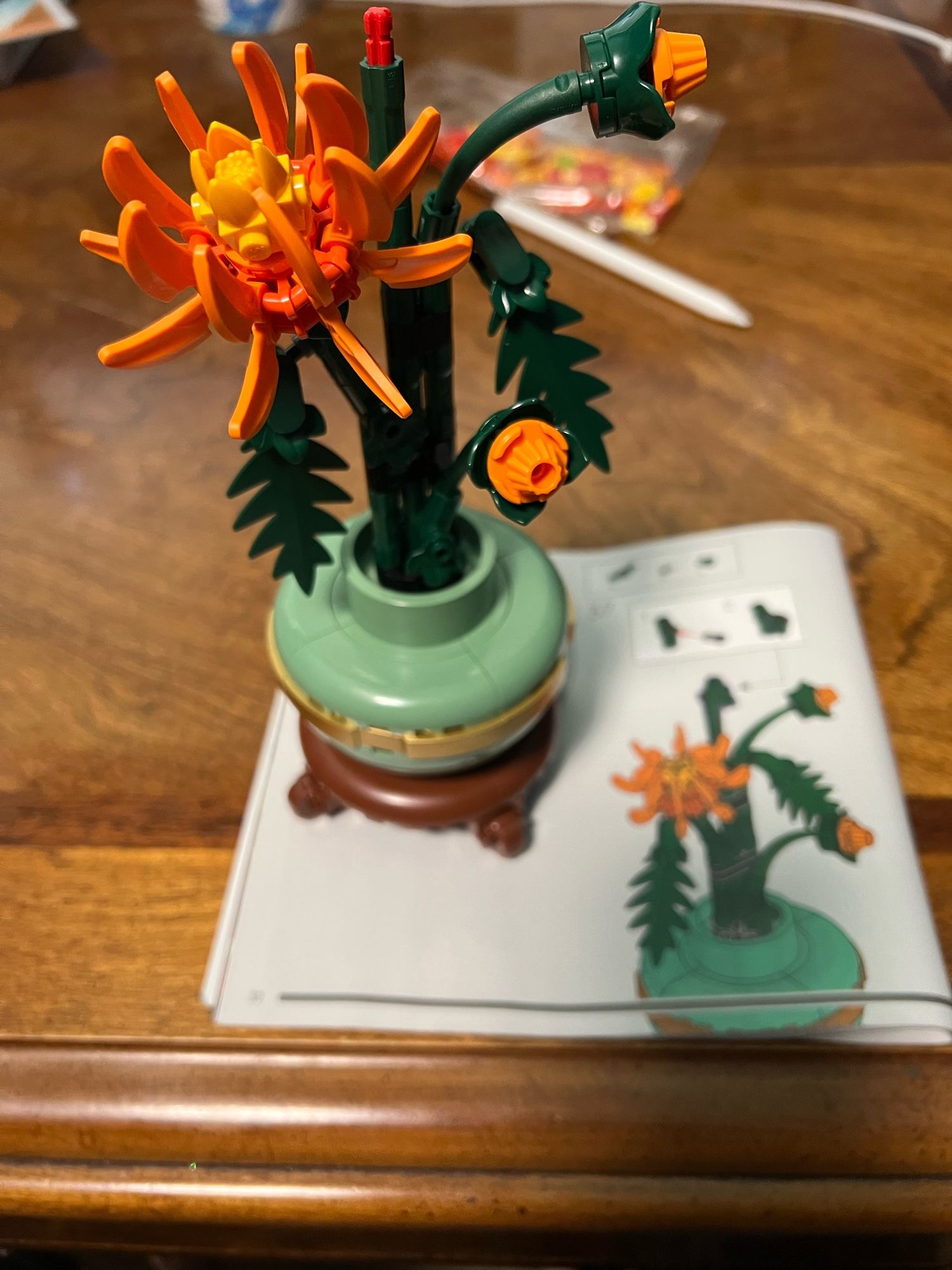 The photo shows the green & brown base of the LEGO Chrysanthemum build with added greenery & a few orange & yellow flower buds. This is bag 2.