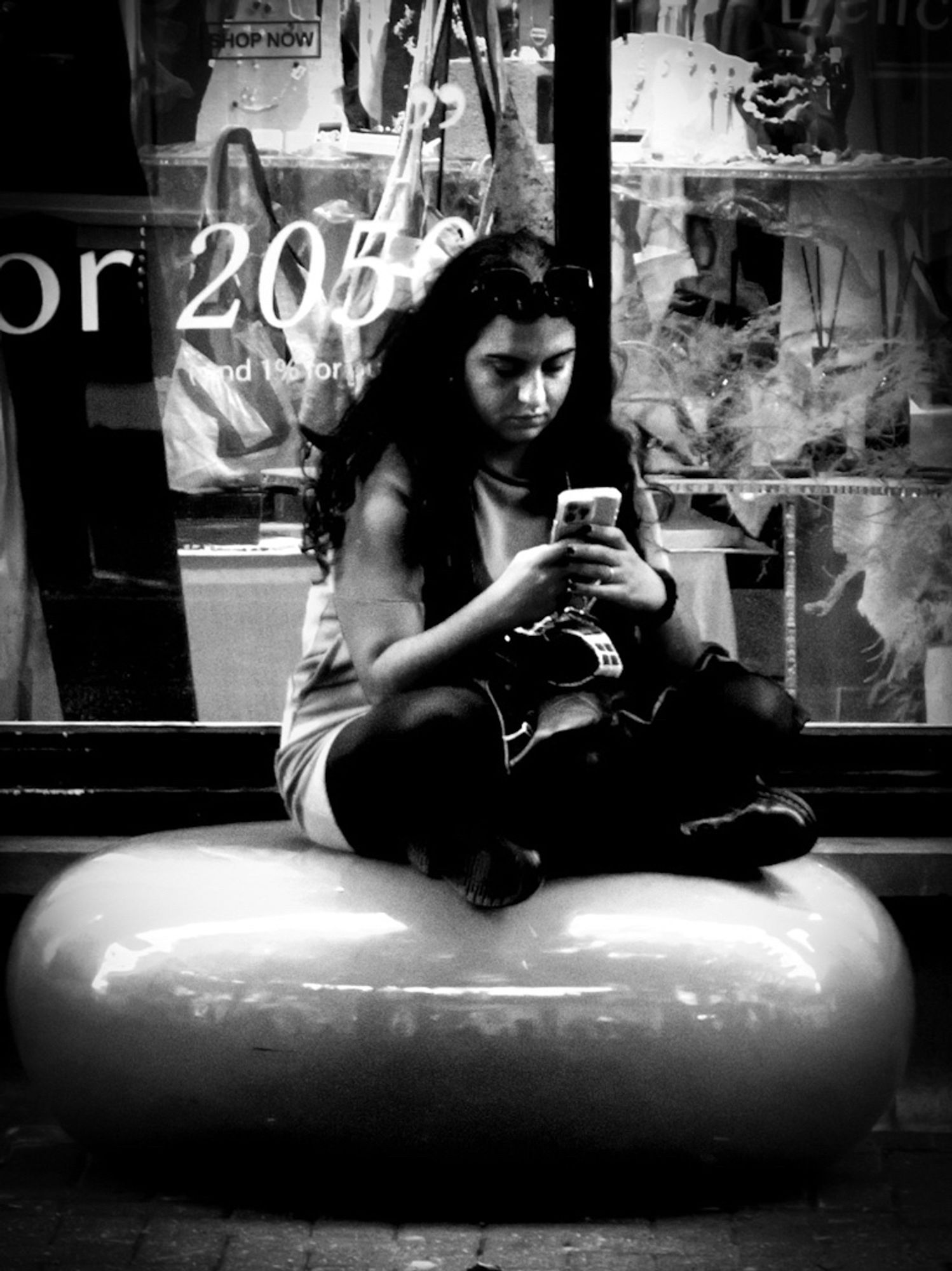 A high contrast black and white photo of a young woman sitting cross-legged on a polished round stone seat.