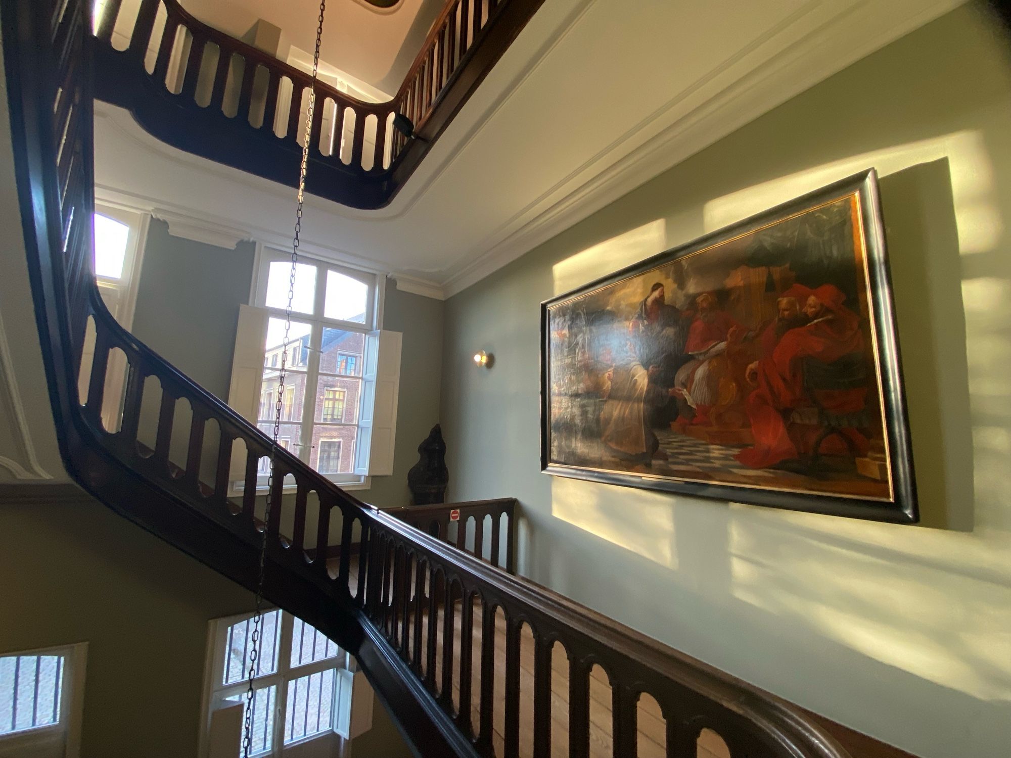 The entry hall of the museum with two large windows and a beam of light coming in and shining on the painting next to the staircase