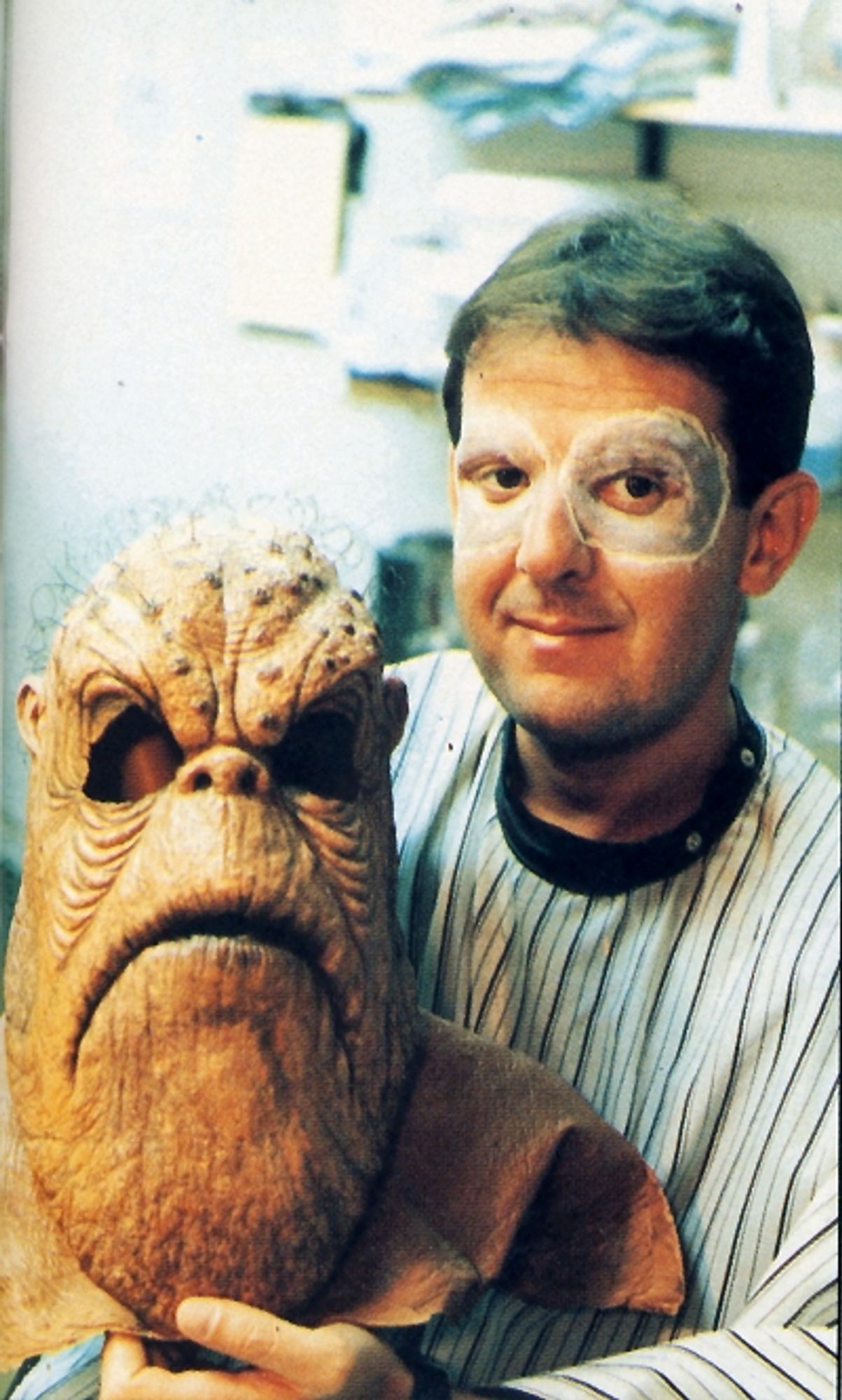 Morn actor Mark Allen Shepherd of DS9 holds his mask at his side to show his face and Morn eye makeup