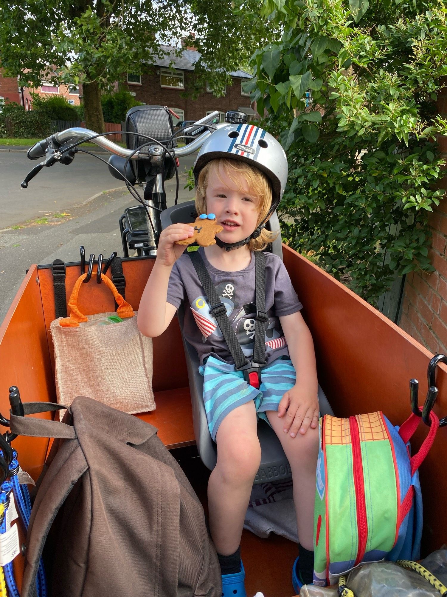 Boy in the same trike, holding up a home-made gingerbread person with blue Smarties for eyes.