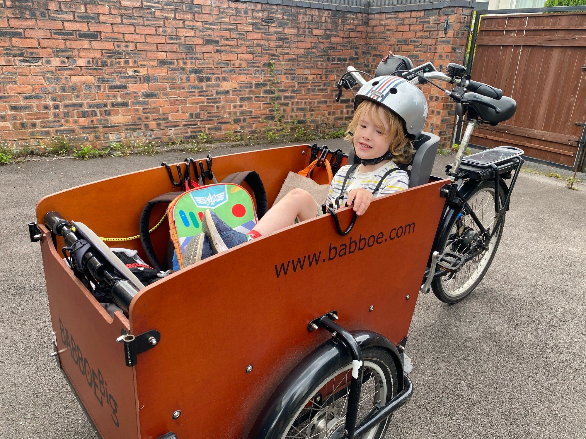 Boy sitting in the wooden box at the front of a cargo trike. It's a Babboe Big-E.