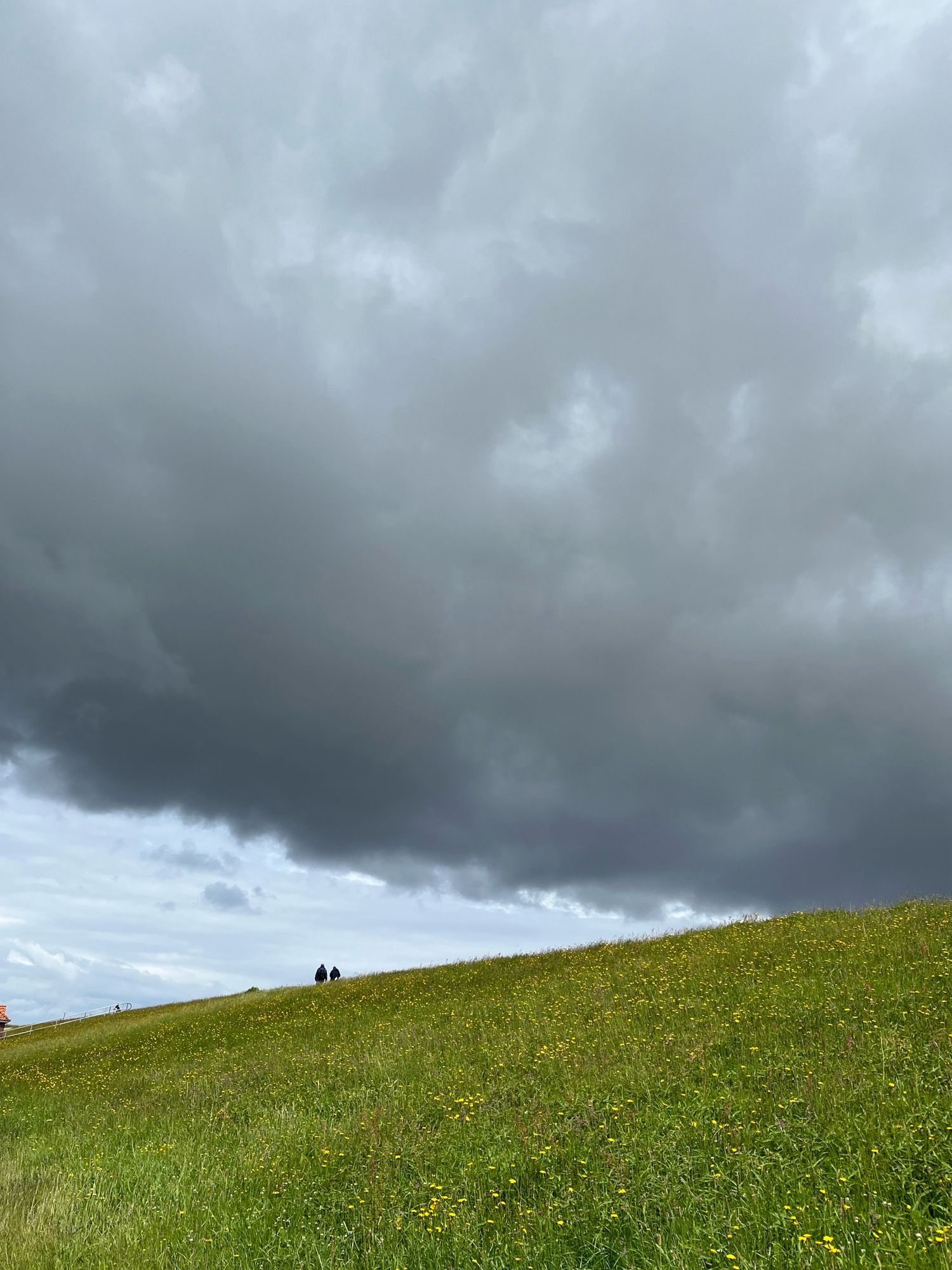 Zwei Personen auf dem Deich, am Himmel eine massive Regenwand