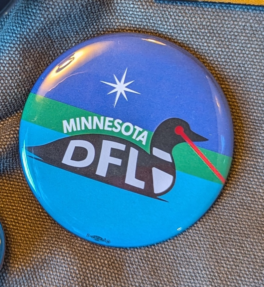 A pin on button with a simple drawing of a loon with a laser eye and a North Star behind it. It says "Minnesota" above the loon and the body of the loon says "DFL".