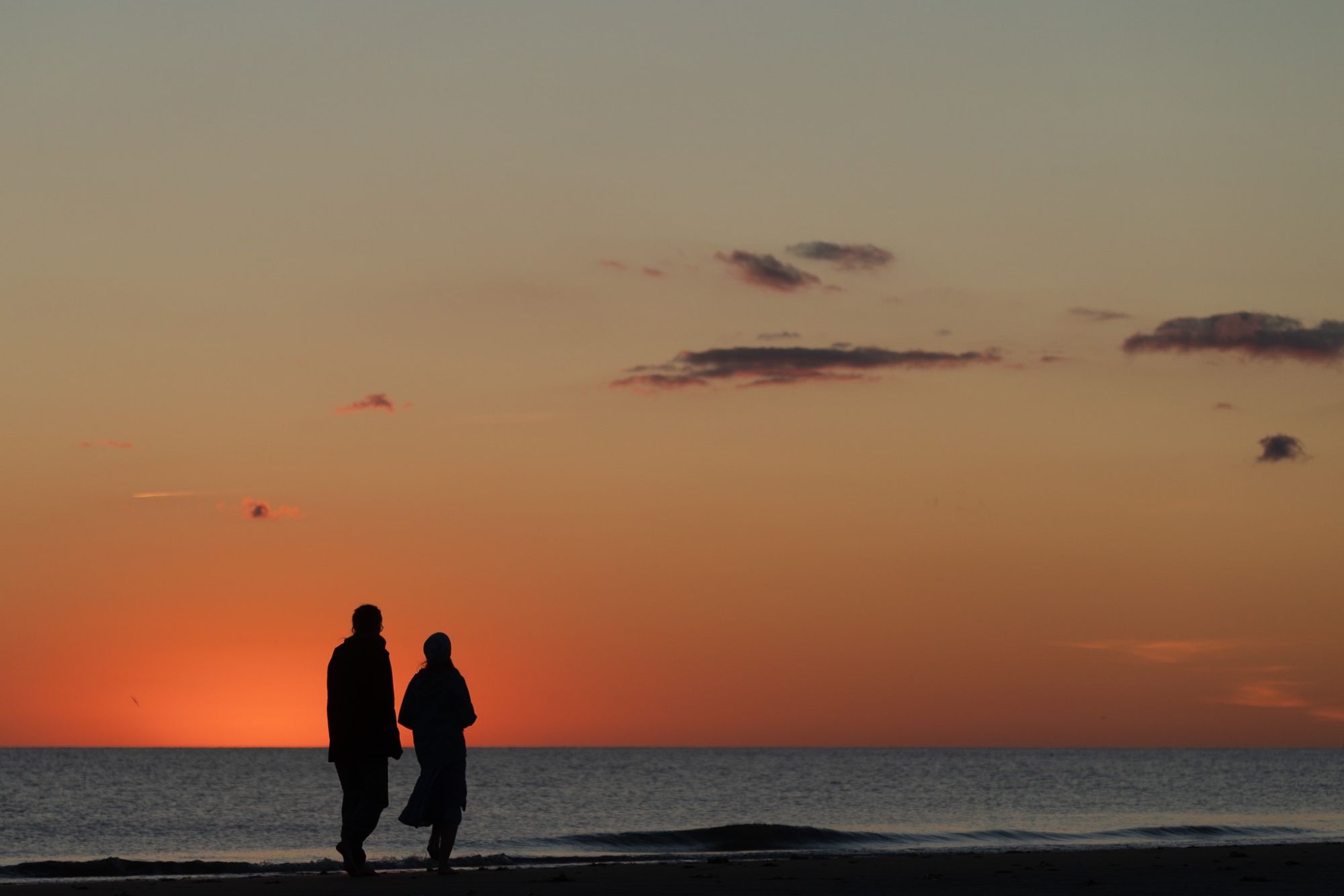 Mutter und Tochter beim Spaziergang am Nordseestrand nach Sonnenuntergang. Im Hintergrund Abendrot.