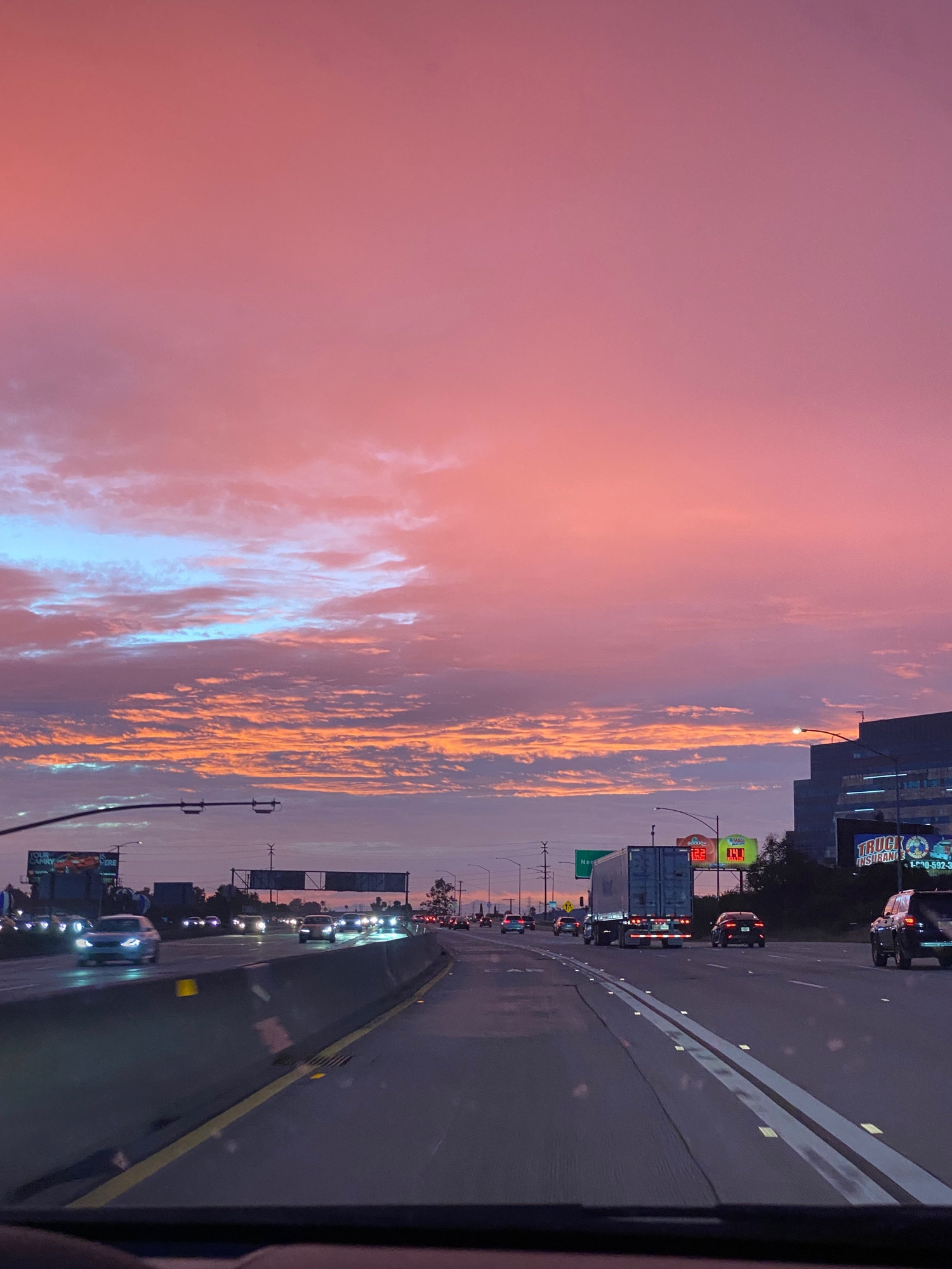 Pink sky with sun reflecting orange on the clouds over the freeway in Los Angeles