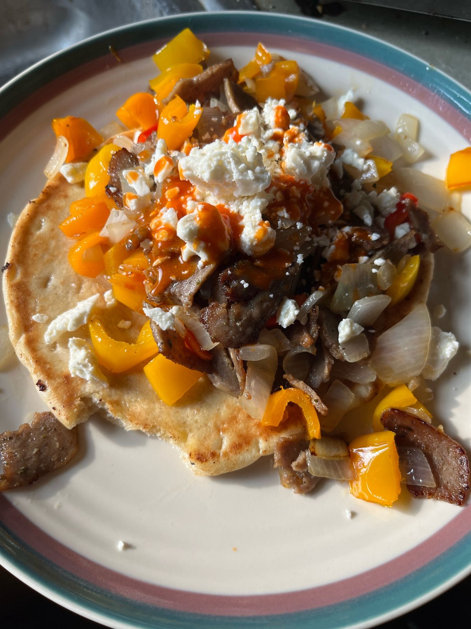 A slice of fried pita bread with chopped peppers, lamb, raw onion, and feta cheese