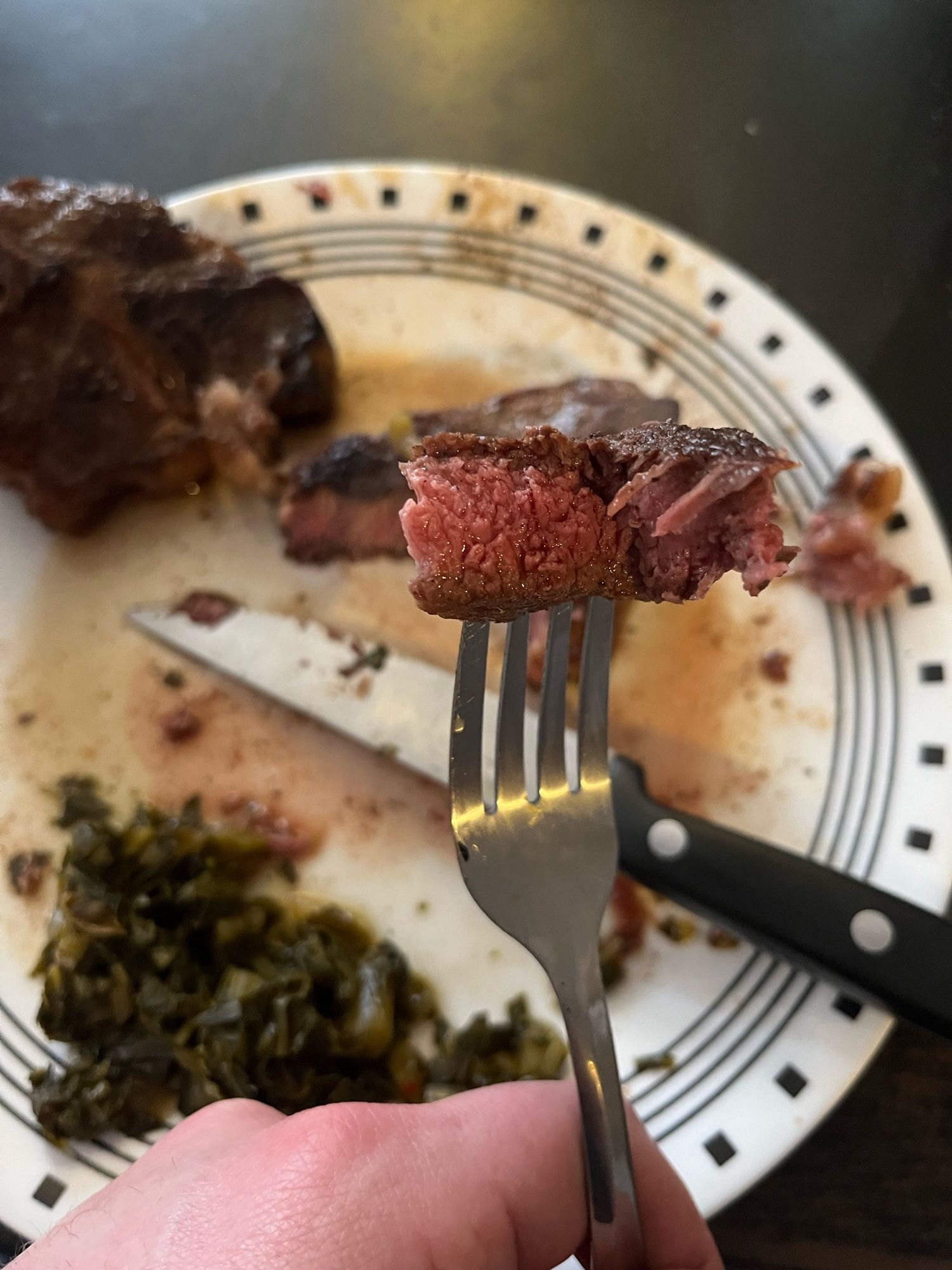 A fork holding up a cut of rare lamb with some greens on the plate