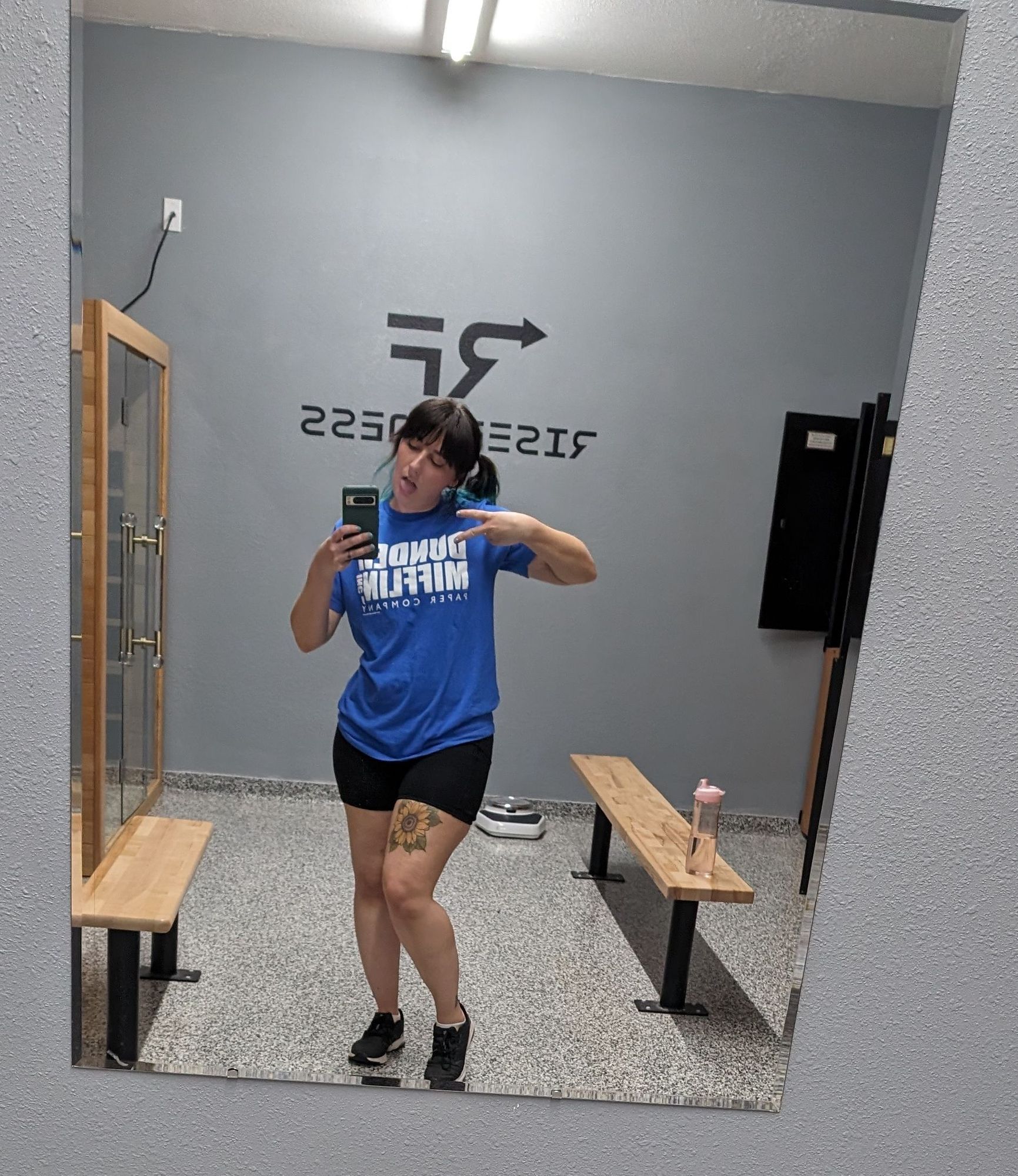 A mirror selfie of me at the gym. I'm wearing a blue dunder Mifflin shirt with my hair in pigtails and black bike shorts and black Nikes. My tongue is sticking out.