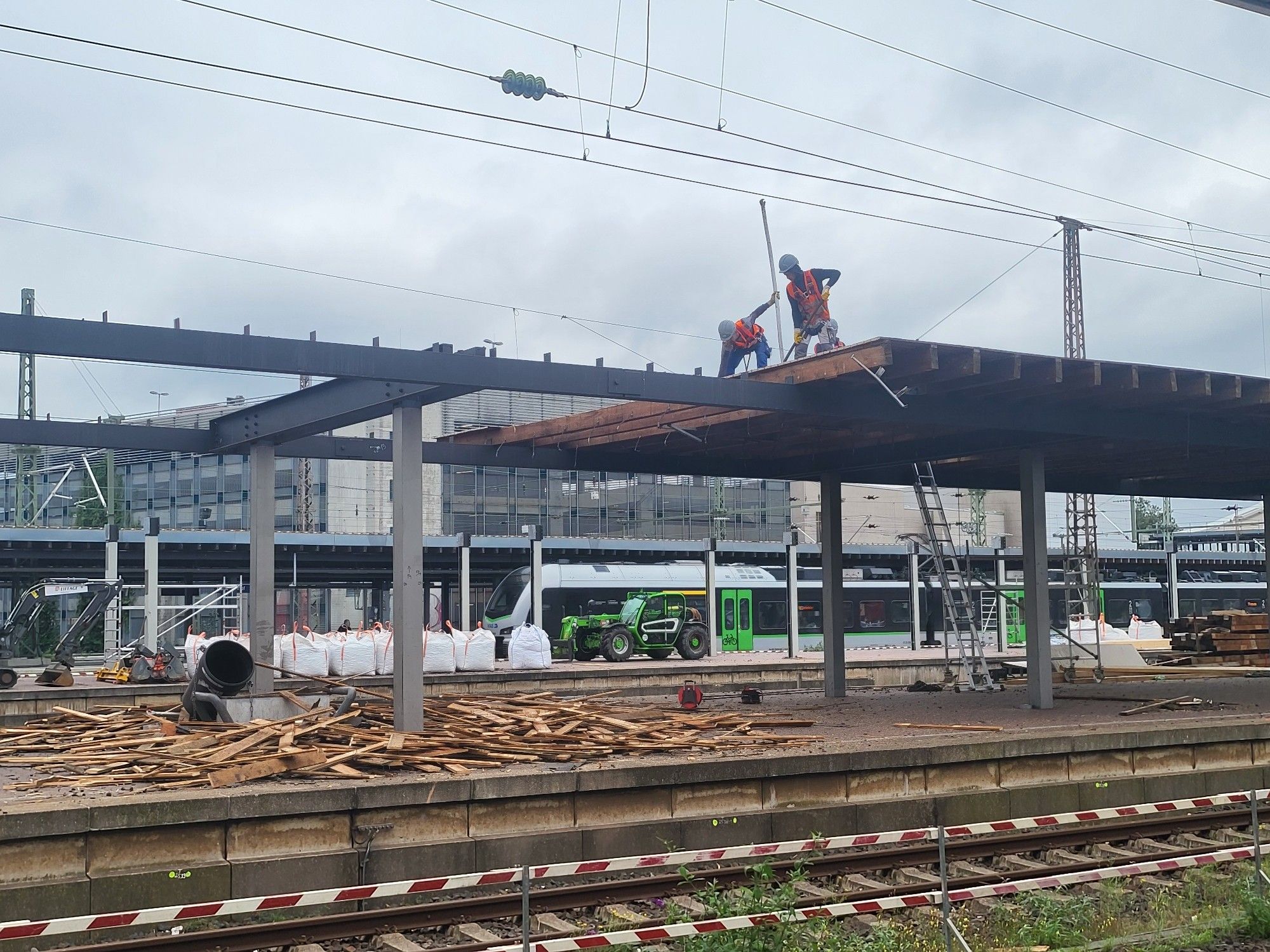 Auf dem Dach eines Bahnsteigs reißen Bauarbeiter mit orangen Westen Teile aus der Konstruktion und lassen sie auf den Haufen am Boden fallen.