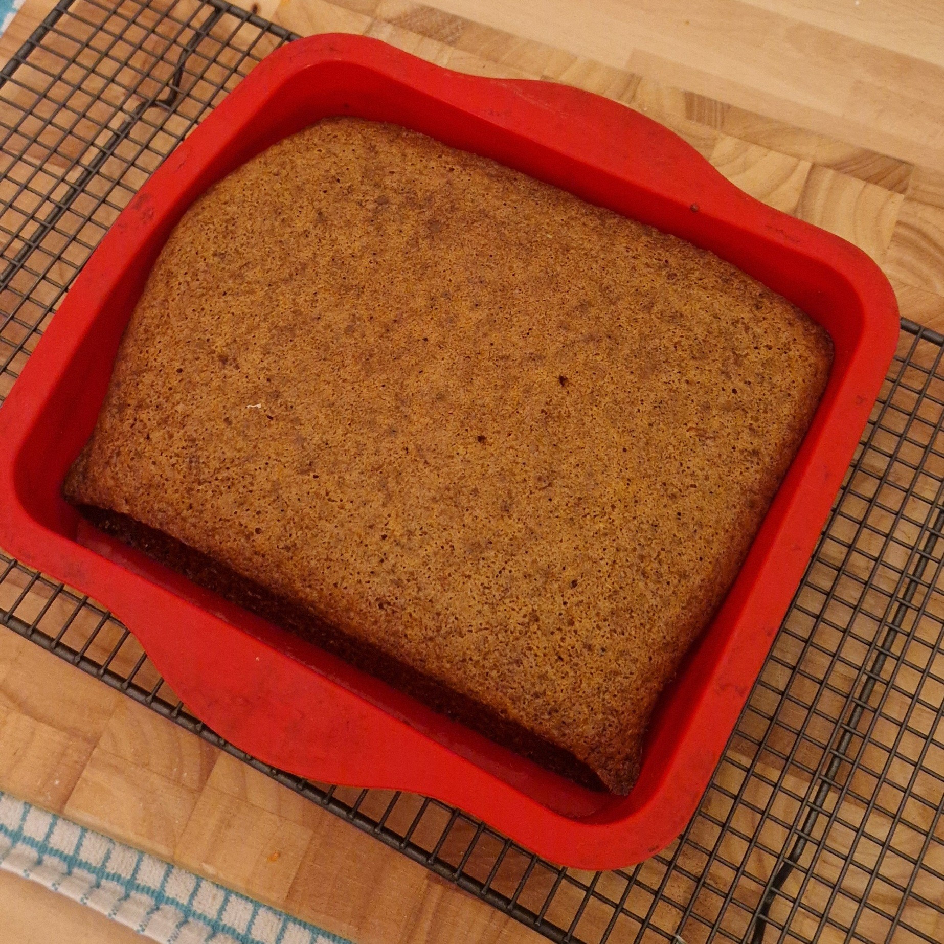 A carrot cake in a red silicone baking tray on a cooling rack 