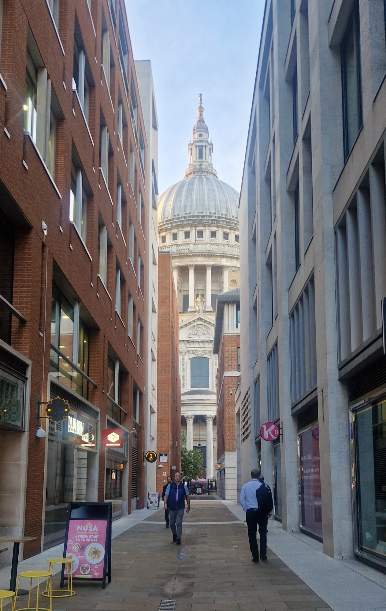 A view of St Paul's cathedral down a narrow pedestrianised street between office buildings with restaurants on the ground floor