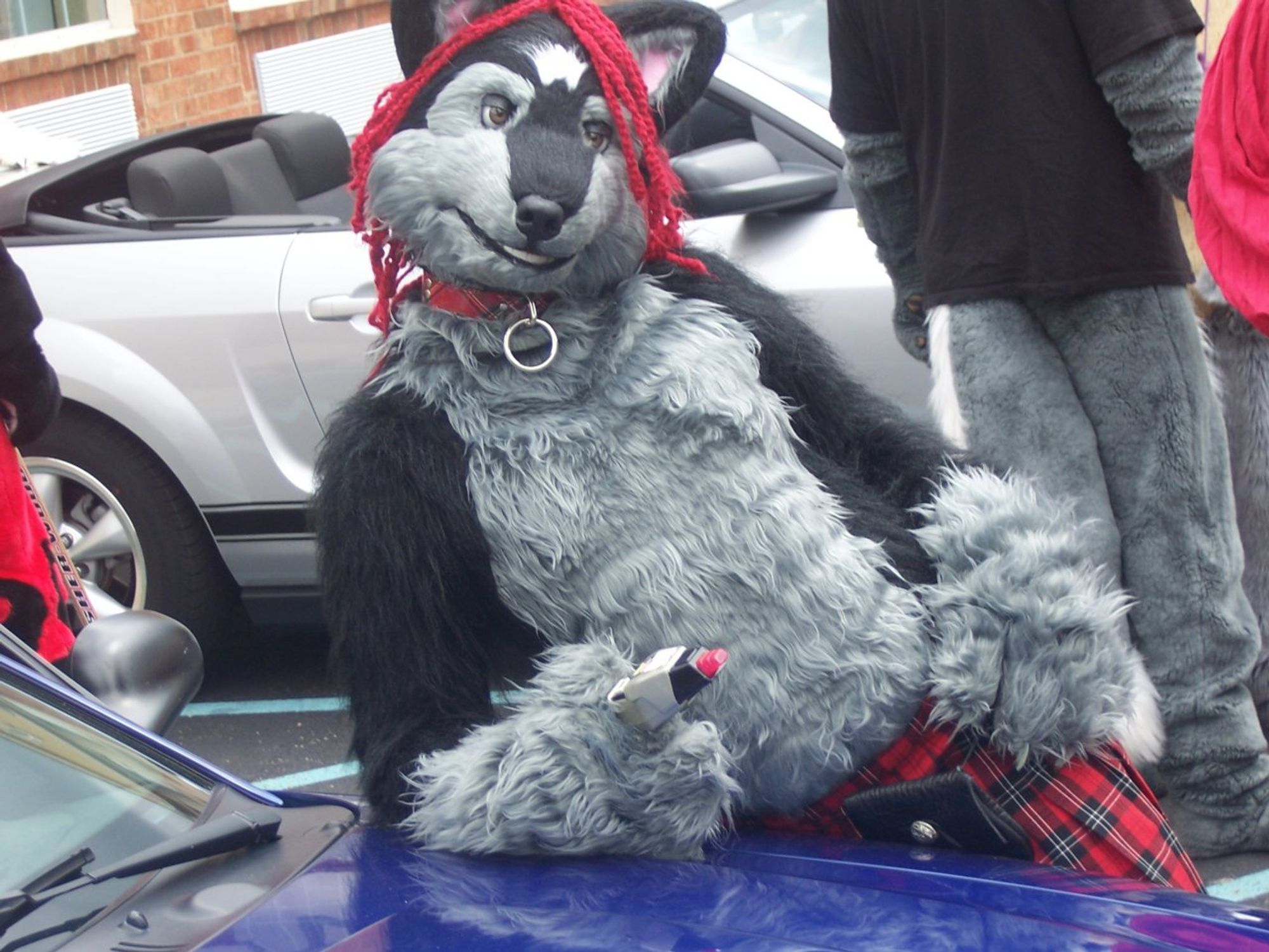 A black and gray furred werewolf with red dreadlocks, a plaid collar, and a kilt leans on a car. He is also holding a Star Trek TNG phaser, because of course I was.