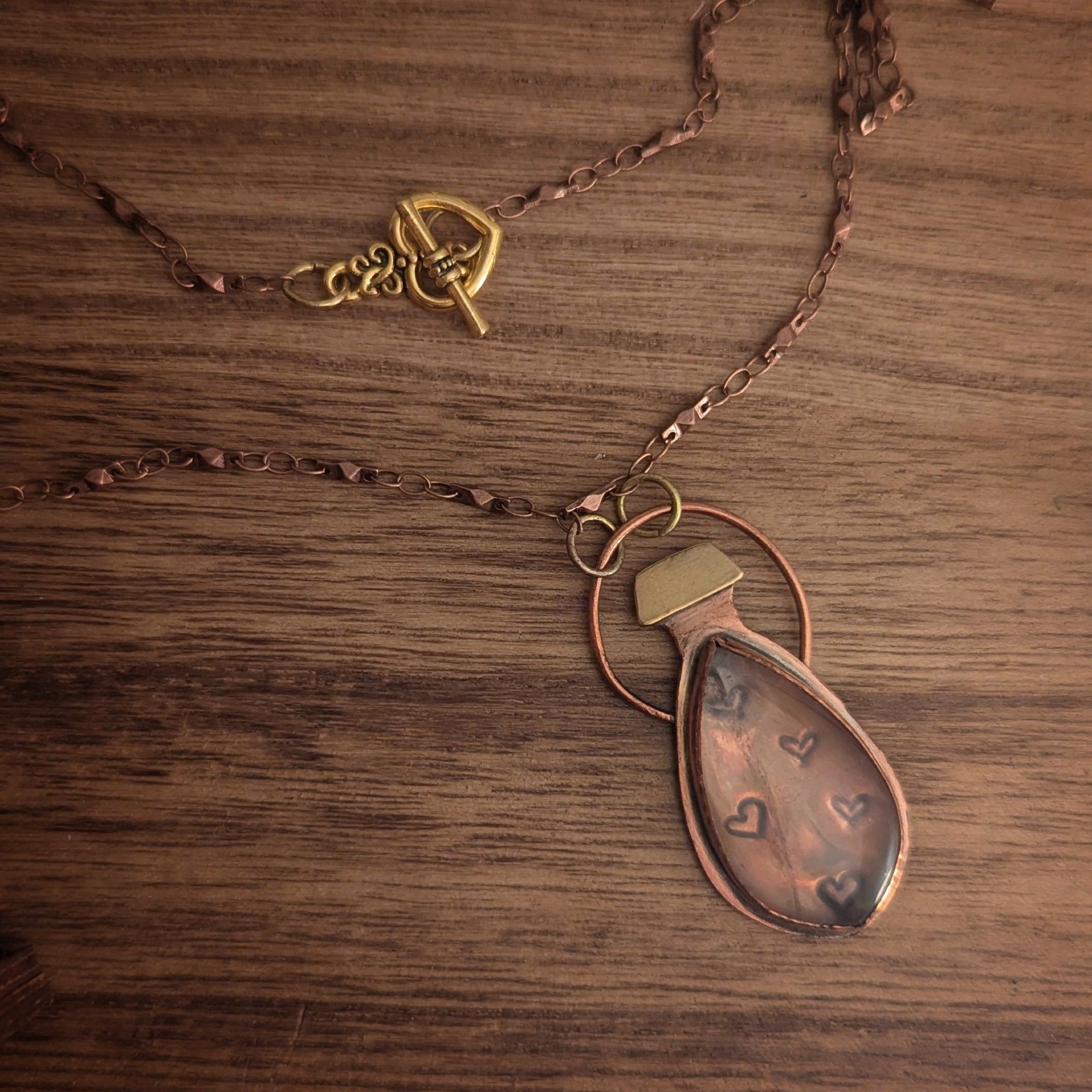 A copper potion bottle necklace with heart bubbles stamped under a rose quartz and gold brass details.