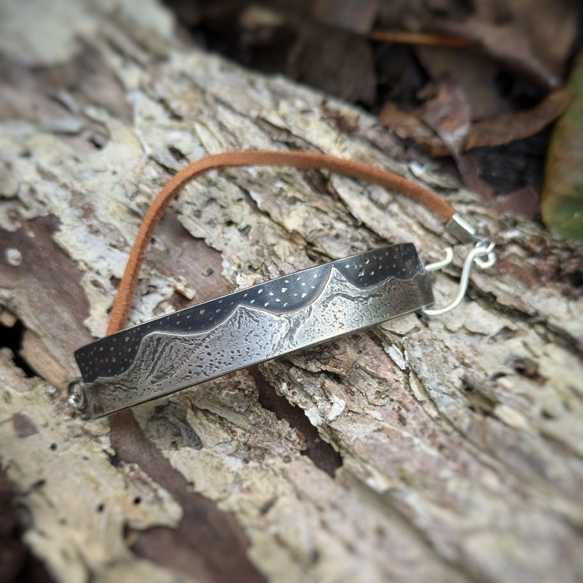 A solid silver bracelet with a mountain scape scene engraved into it under a starry sky.