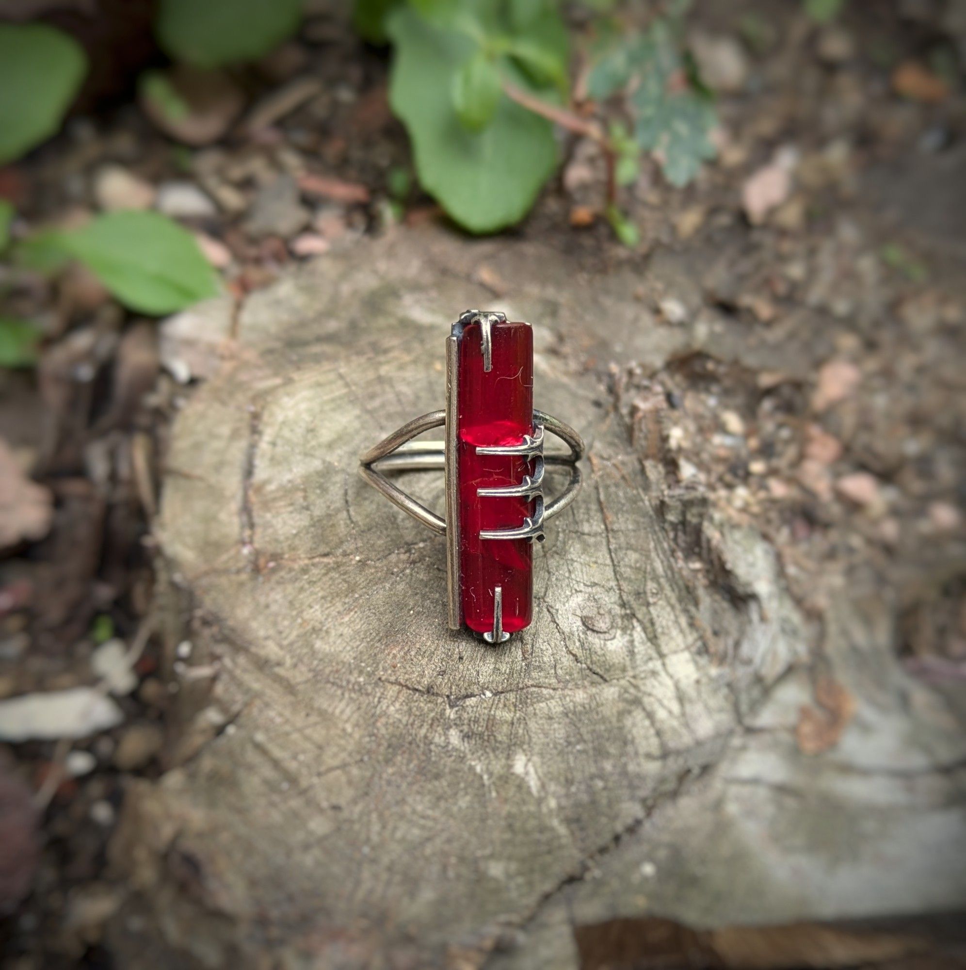 A silver ring has a bright red flag glass set with Gothic style spikes, three on one side and one on each end.