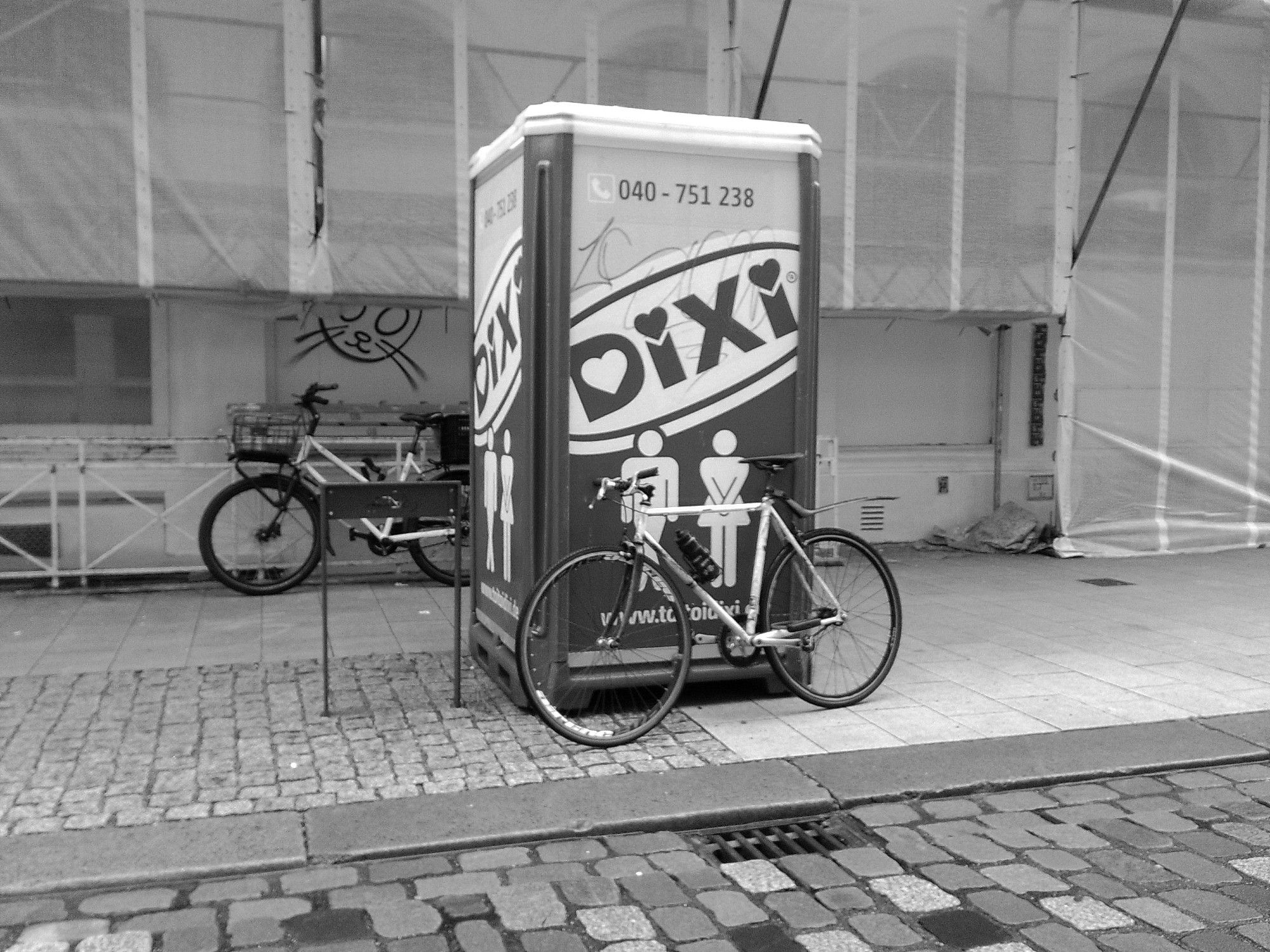 Dixiklo an den ein Fahrrad lehnt. Fotografiert in SW