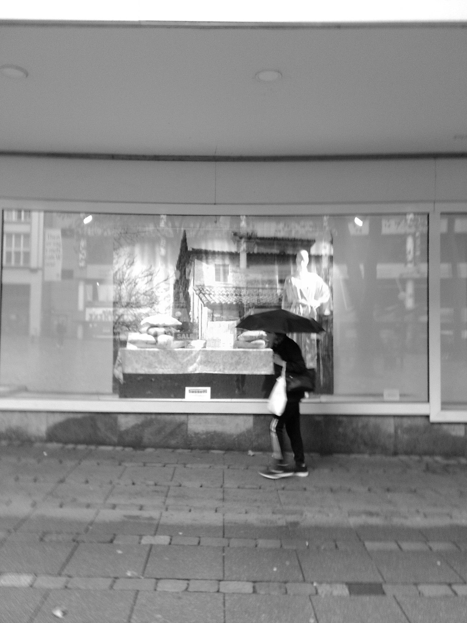 Person mit Regenschirm läuft an Schaufenster vorbei. Fotografiert in SW